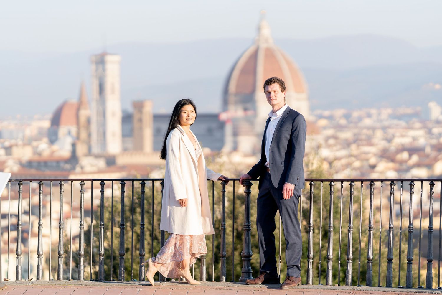 Two people stand on a scenic overlook with Florence's iconic Duomo cathedral and cityscape in the background.