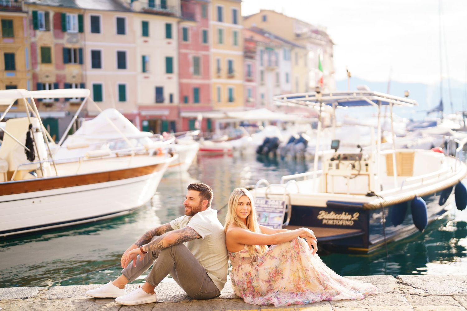 Couple relaxing together by boats docked along colorful Italian coastal buildings in Portofino.