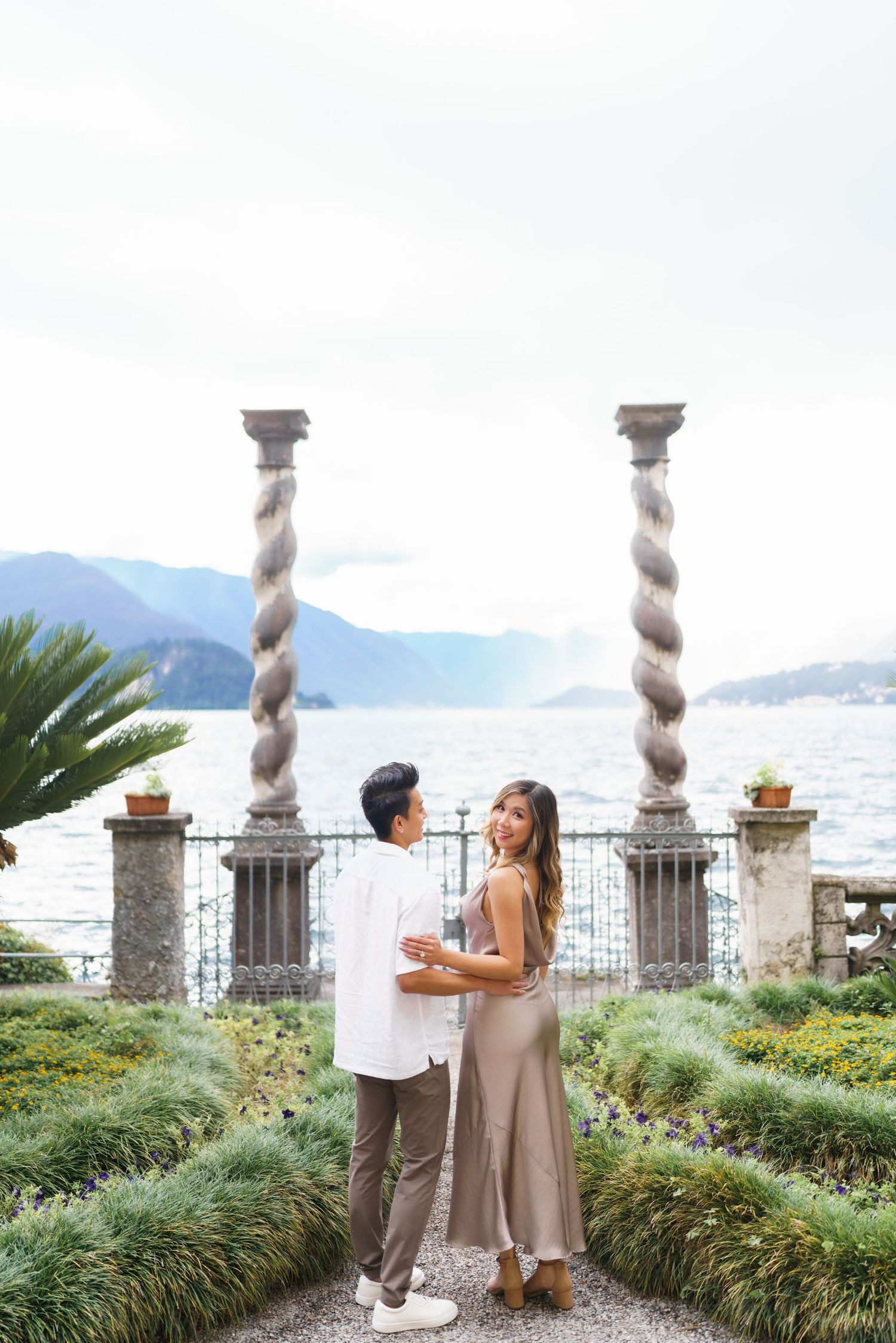A couple shares a romantic moment on an elegant terrace overlooking a coastal mountain landscape.