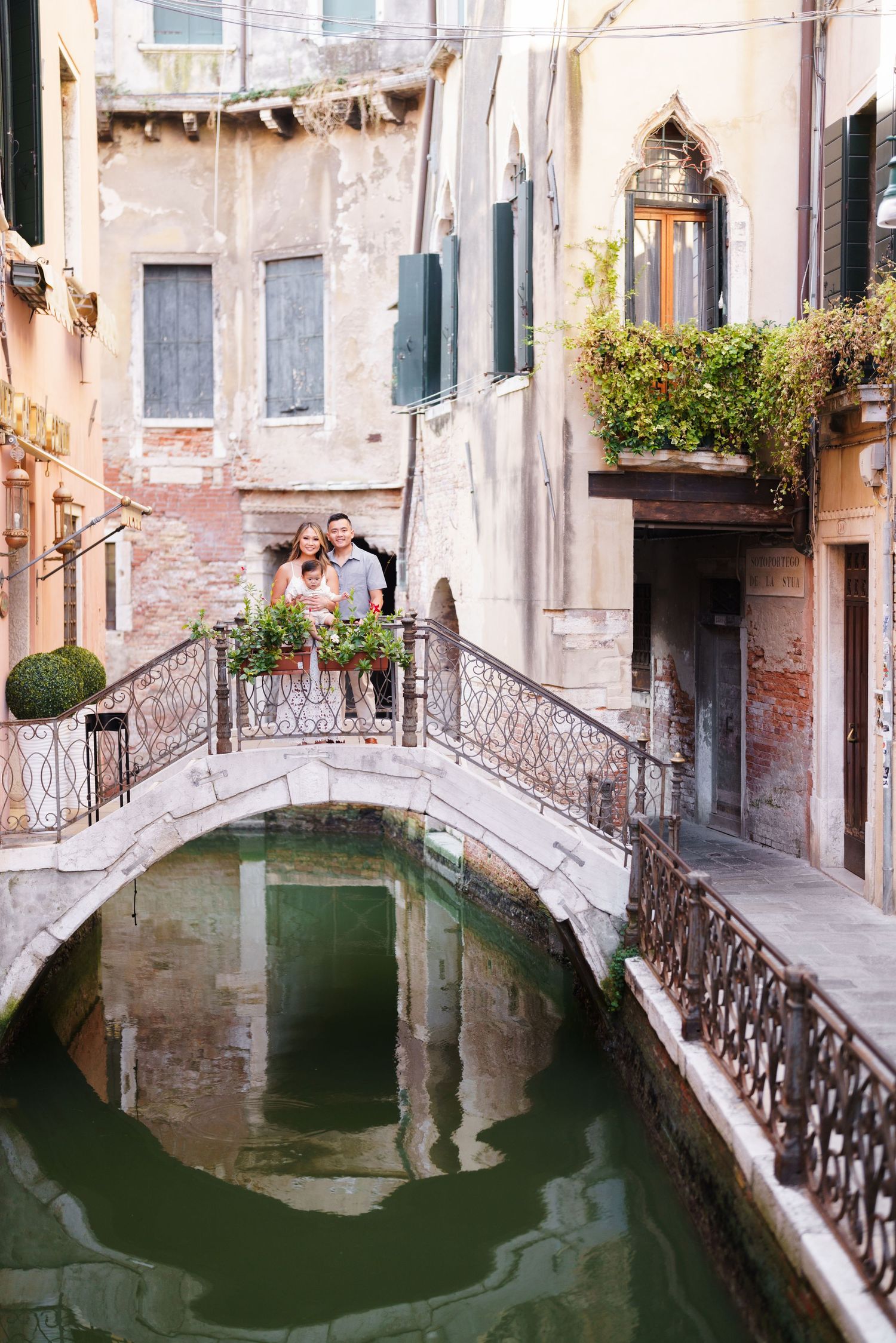 Romantic couple embracing on a charming stone bridge over a green canal in Venice, Italy, surrounded by historic buildings.