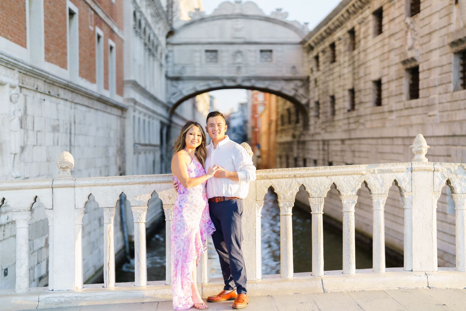 Couple posing on a bridge in Venice, Italy, with the iconic Bridge of Sighs in the background.
