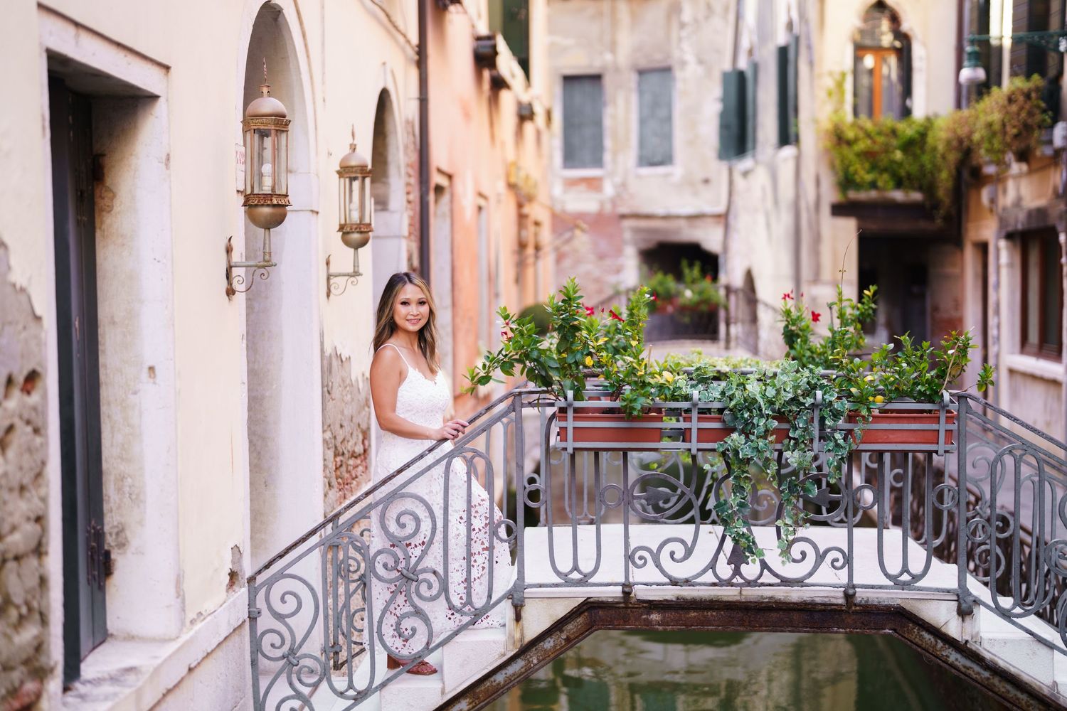 Young woman in white dress posing on ornate bridge over canal in Venice, Italy, surrounded by colorful buildings.