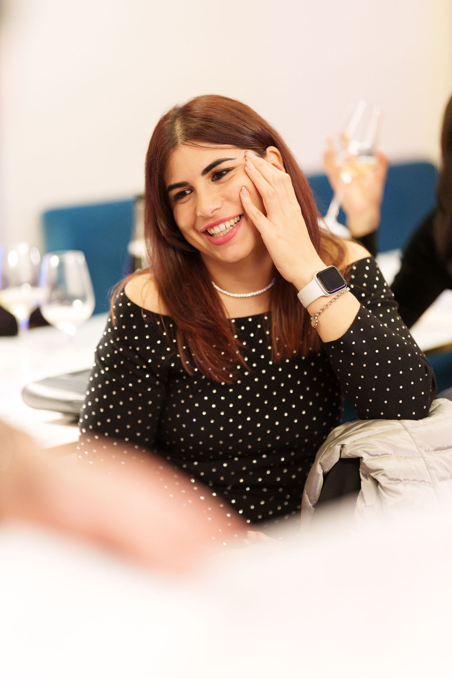 Smiling young woman in polka dot top resting hand on cheek at elegant dining table with wine glasses.