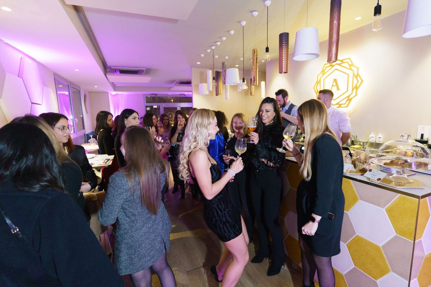 Women socializing at an upscale restaurant event, holding wine glasses amid warm purple ambient lighting.