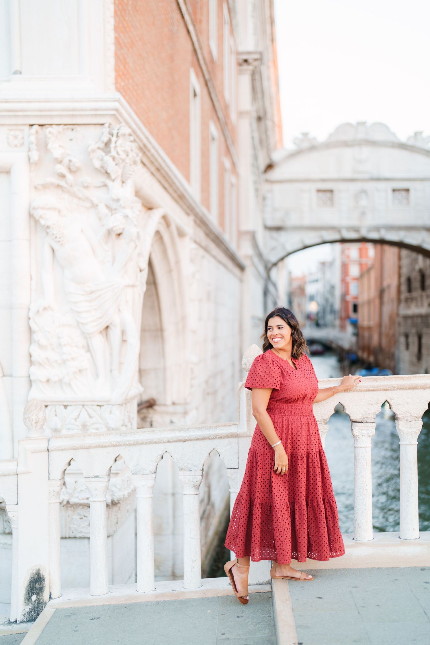 Woman in red dress posing near Bridge of Sighs in Venice, Italy, with canal and historic architecture.