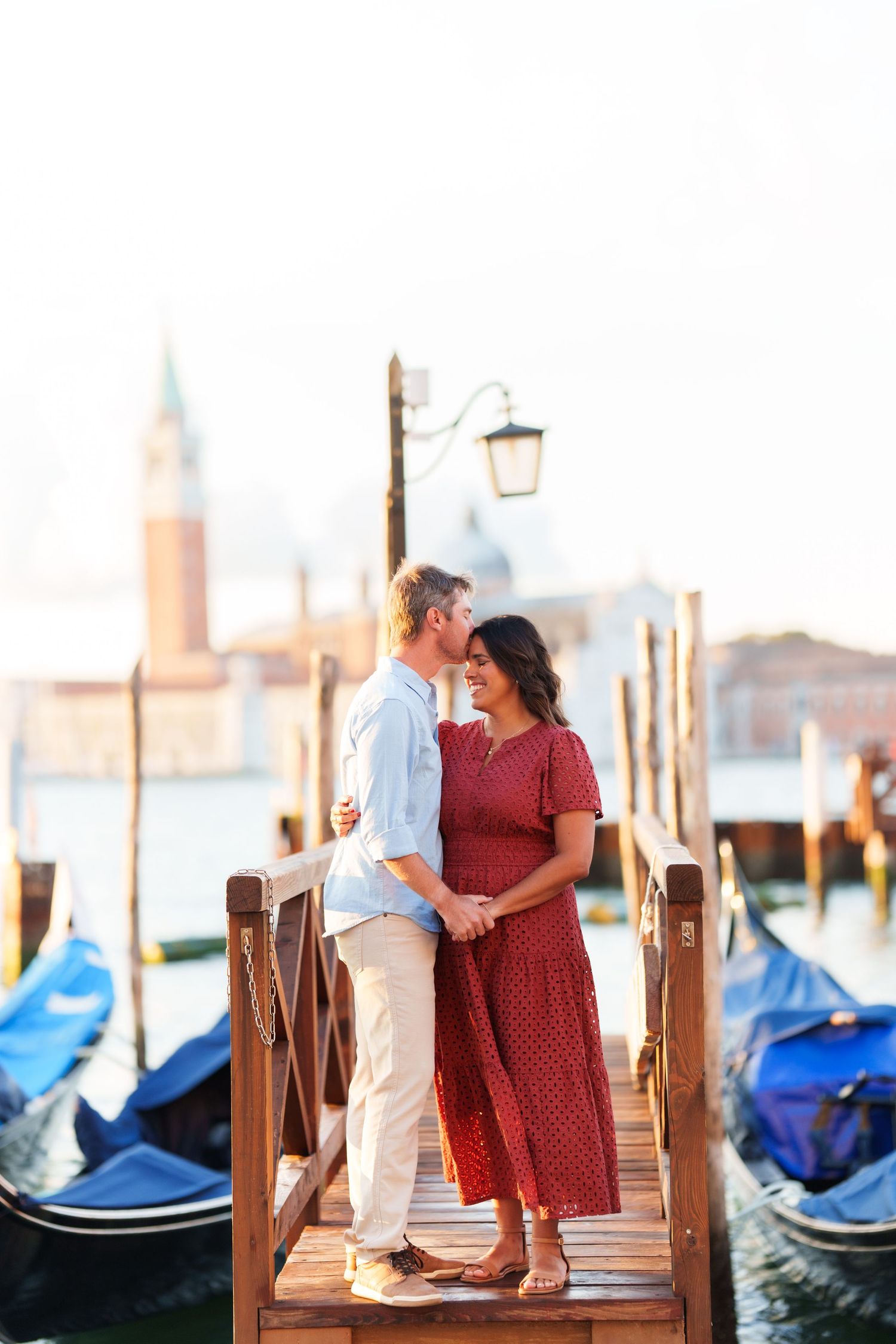 Romantic couple embracing on a wooden dock in Venice, Italy, with gondolas and San Giorgio Maggiore in the background.
