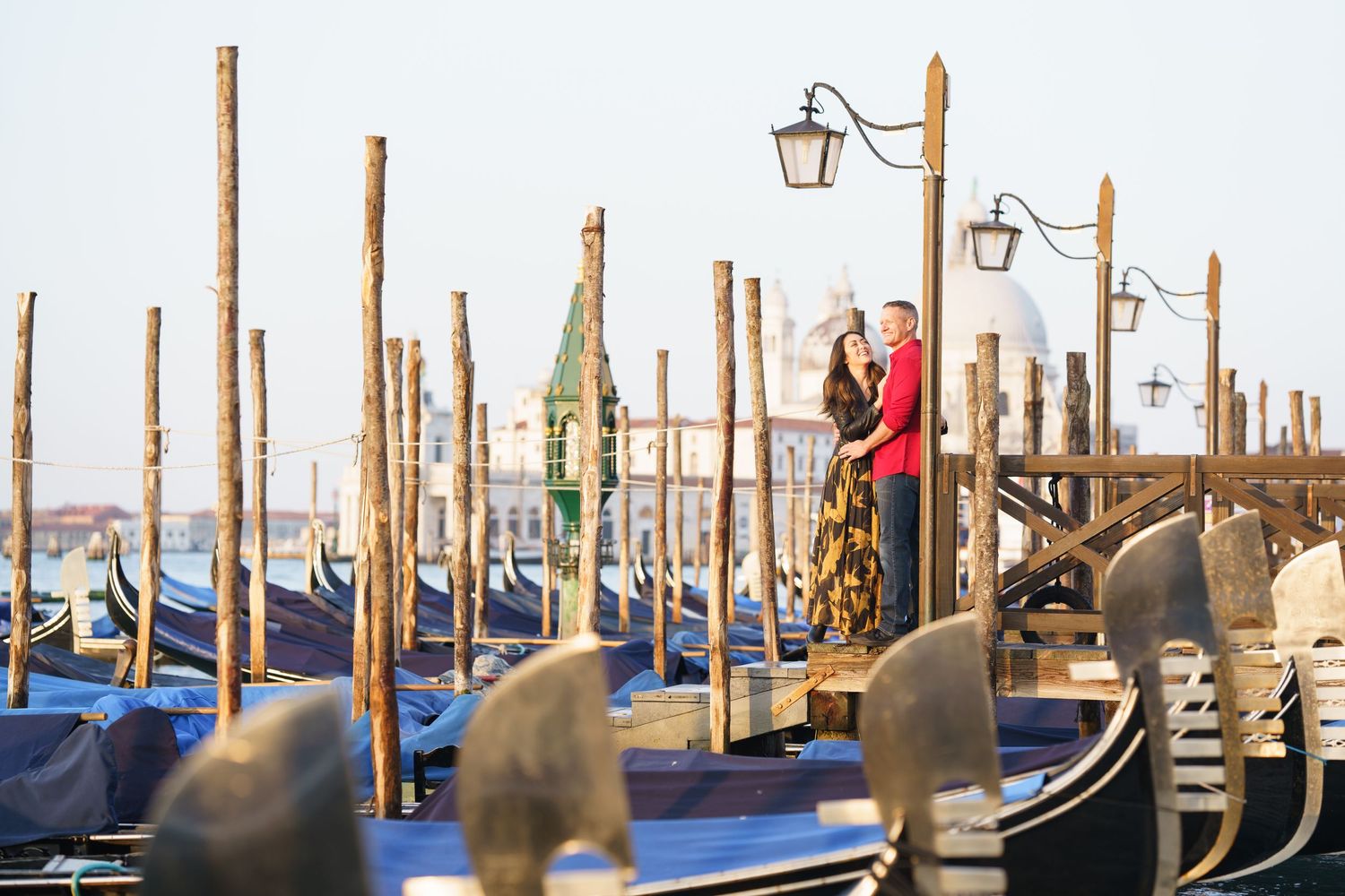Traditional Venetian gondolas moored at wooden posts along the canal with ornate street lamps and waterfront views in Venice, Italy.