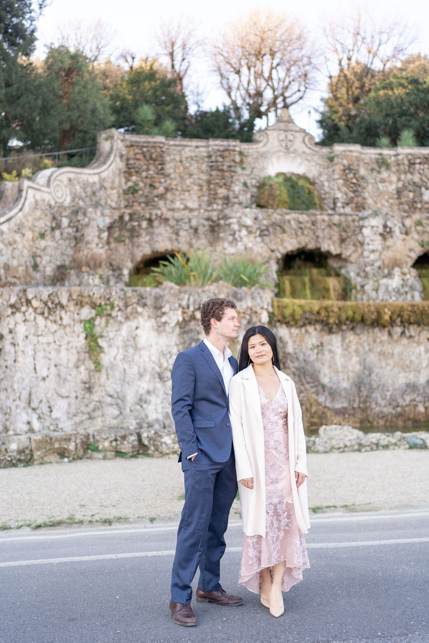 A couple shares a tender moment in front of an old stone wall during an outdoor engagement photo session.