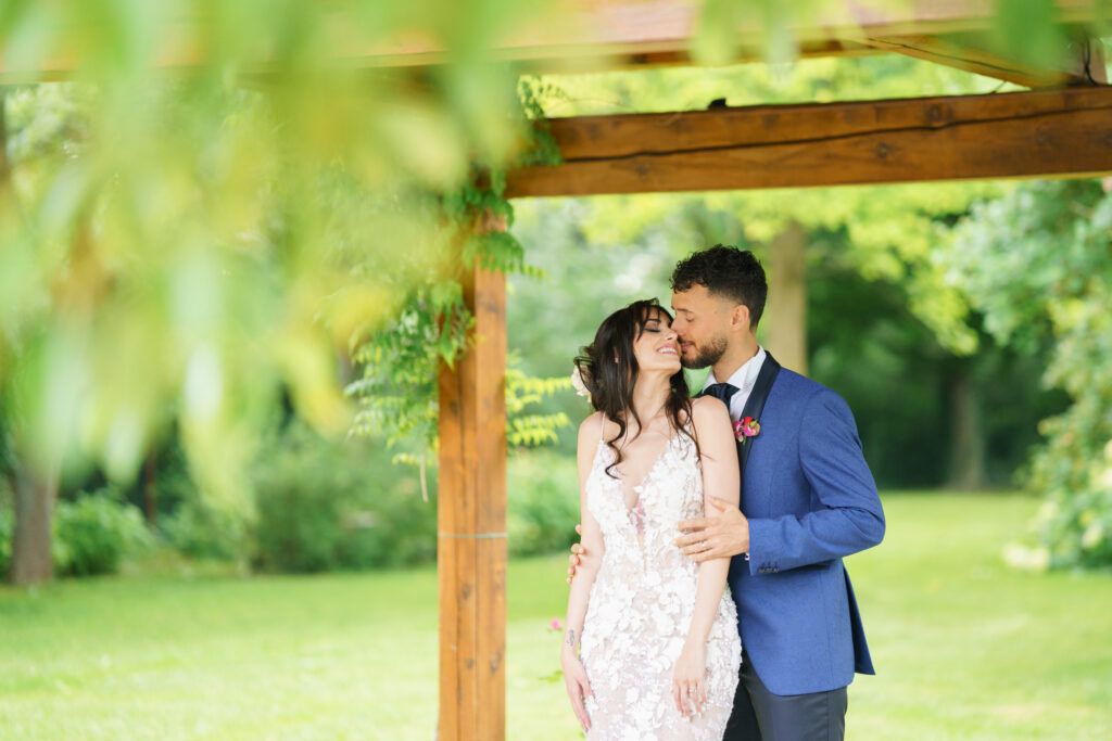Wedding couple posing under a wooden pergola in a lush garden setting.
