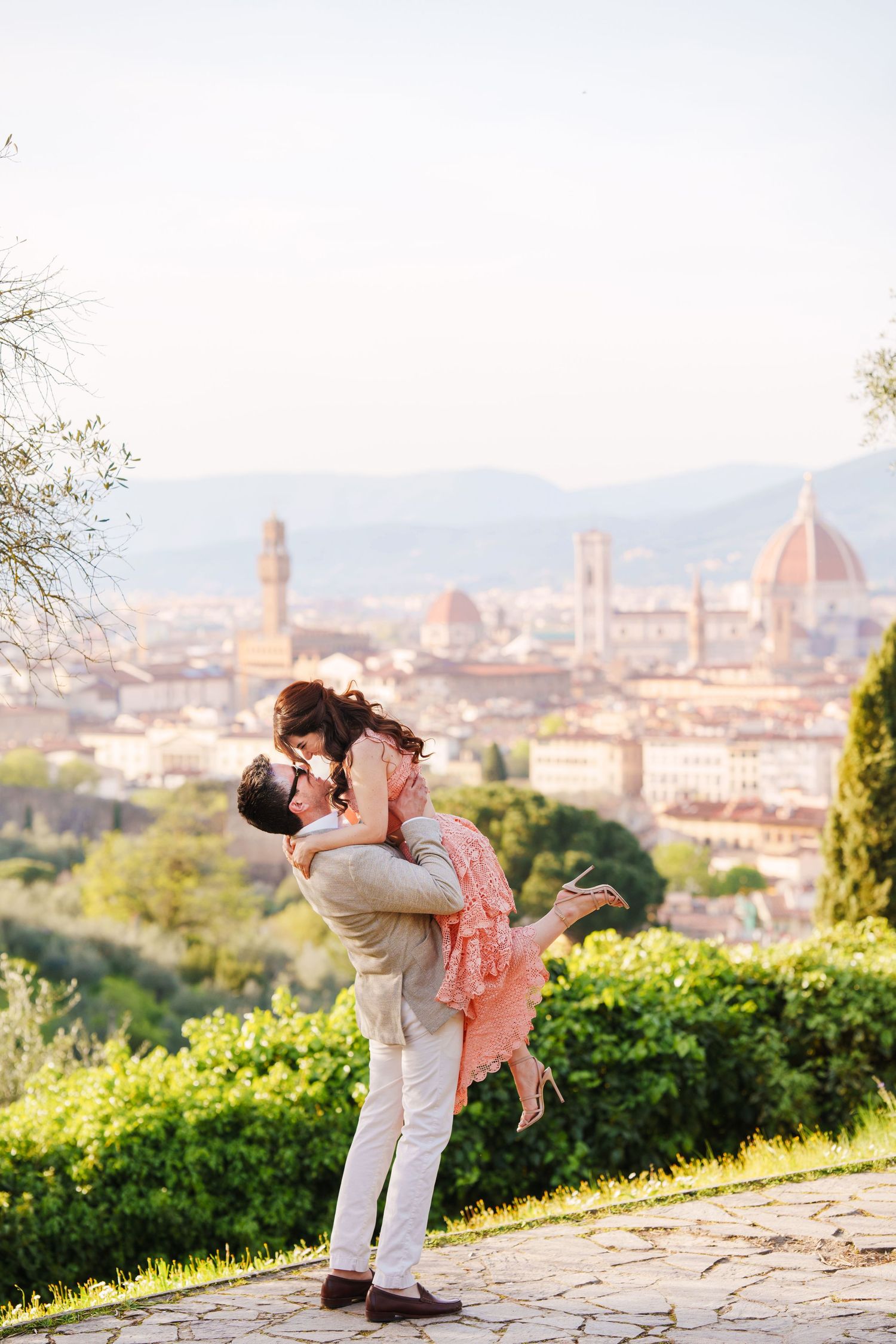 Romantic couple embraces on hilltop overlooking Florence Italy with Duomo cathedral and city skyline in background.
