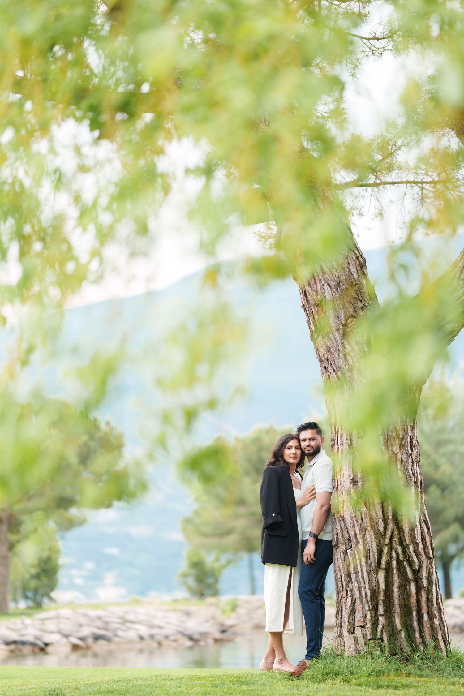 Romantic engagement photo session captured in a series of shots under a large tree with mountain views in the background.
