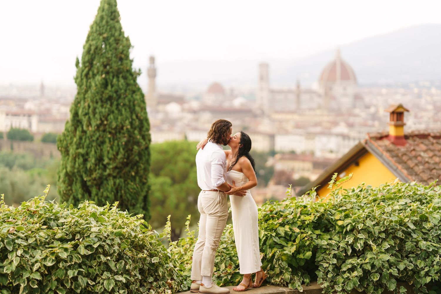 A couple shares a romantic moment overlooking the scenic cityscape of Florence, Italy from a hilltop garden terrace.