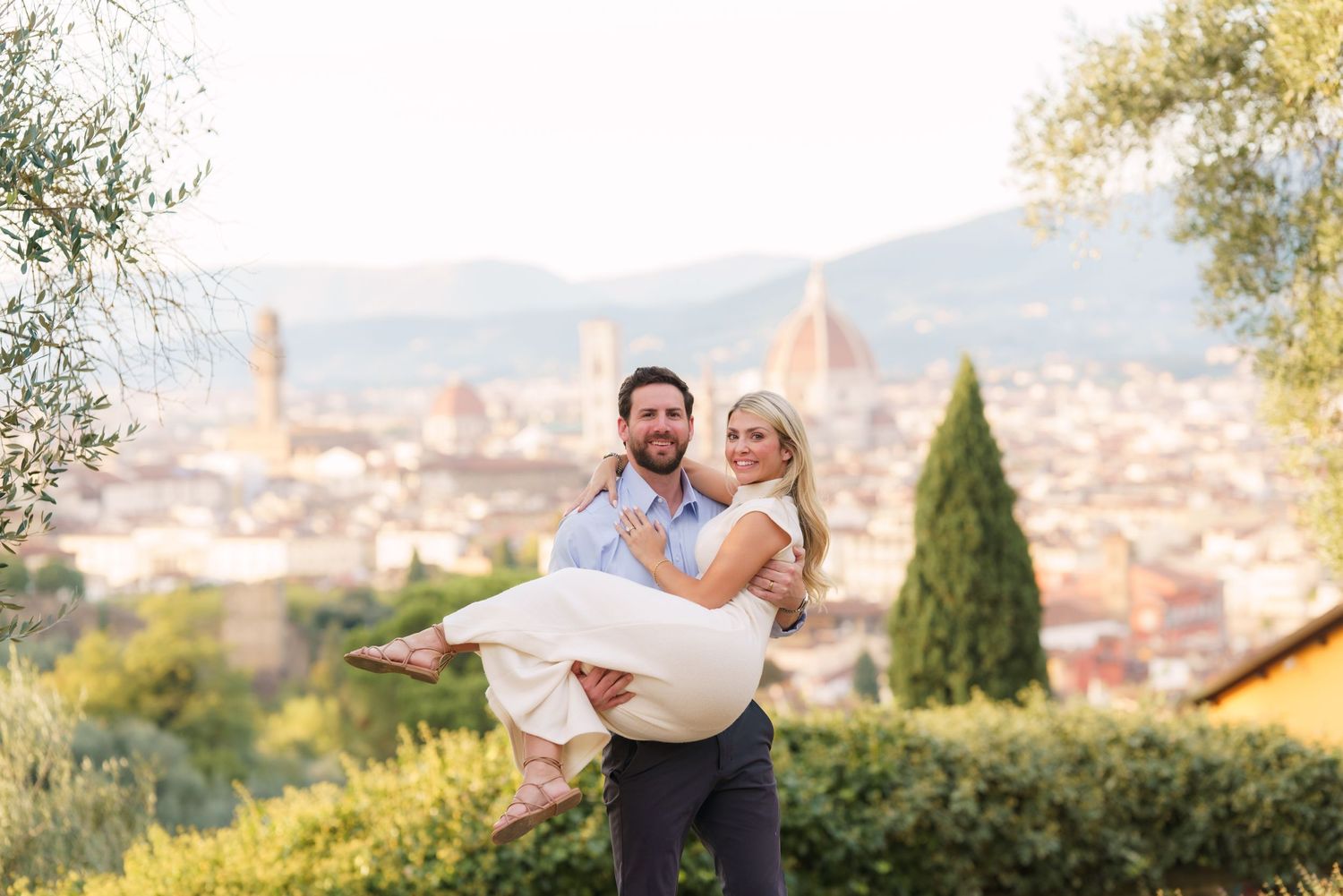 A couple shares a romantic moment overlooking Florence, Italy with the city's iconic Duomo cathedral visible in the background.