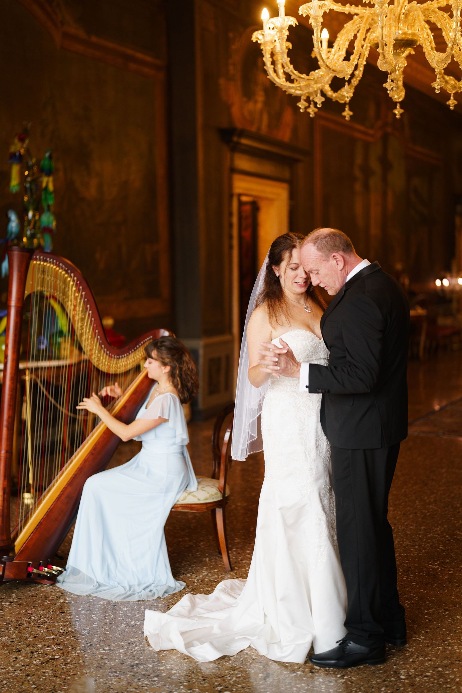 A romantic wedding photoshoot series in an elegant ballroom with a harp and ornate gold chandeliers.