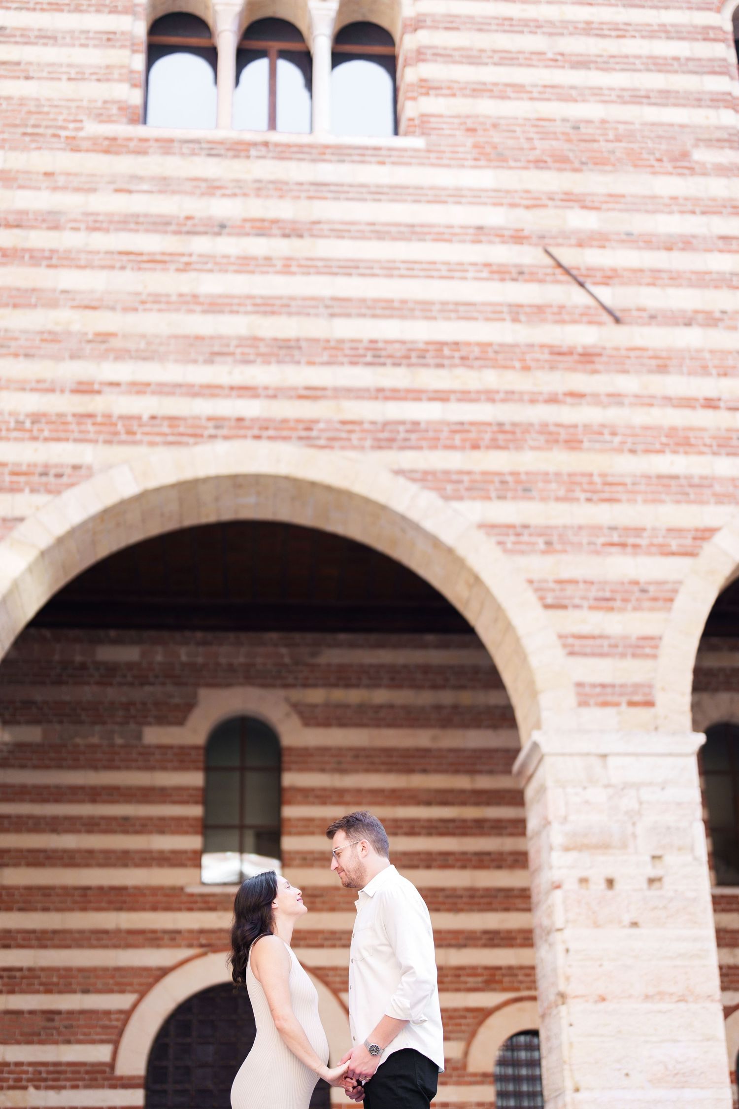 A couple shares a romantic moment under a striped brick archway during a photo session.