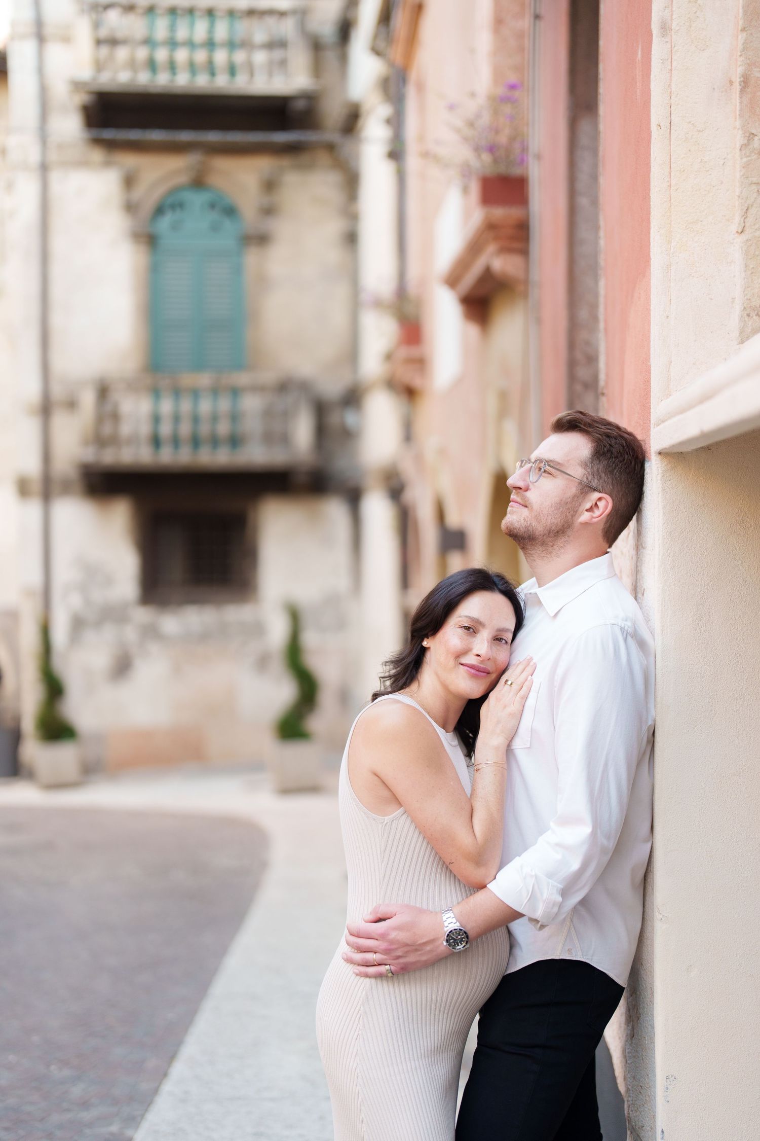 A romantic couple embraces and shares tender moments against a rustic European street backdrop.
