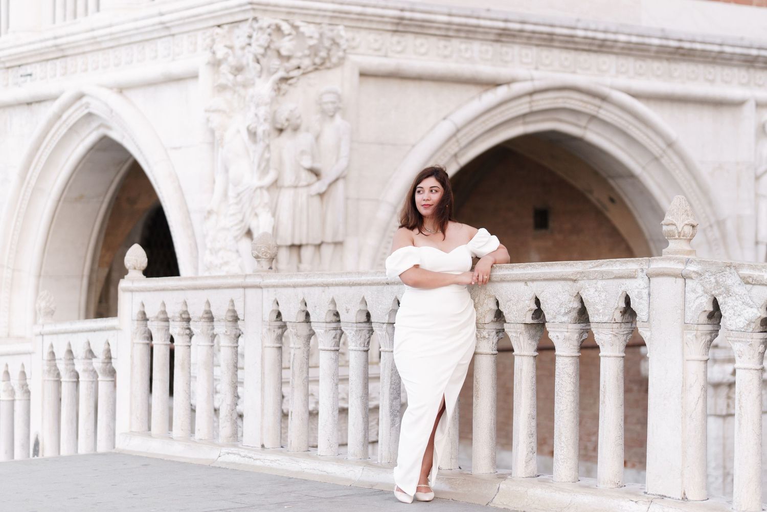A person in a white dress poses along the ornate arches and columns of Doge's Palace in Venice, Italy.