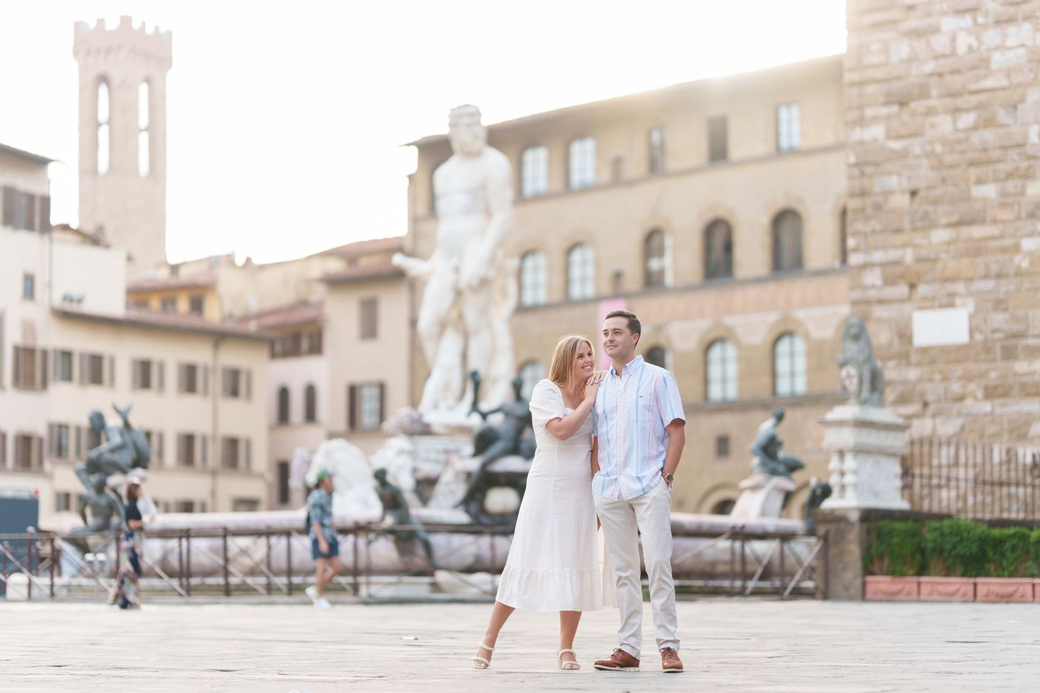 Couple in white outfits walking through historic Italian plaza with stone buildings and statues in Florence.