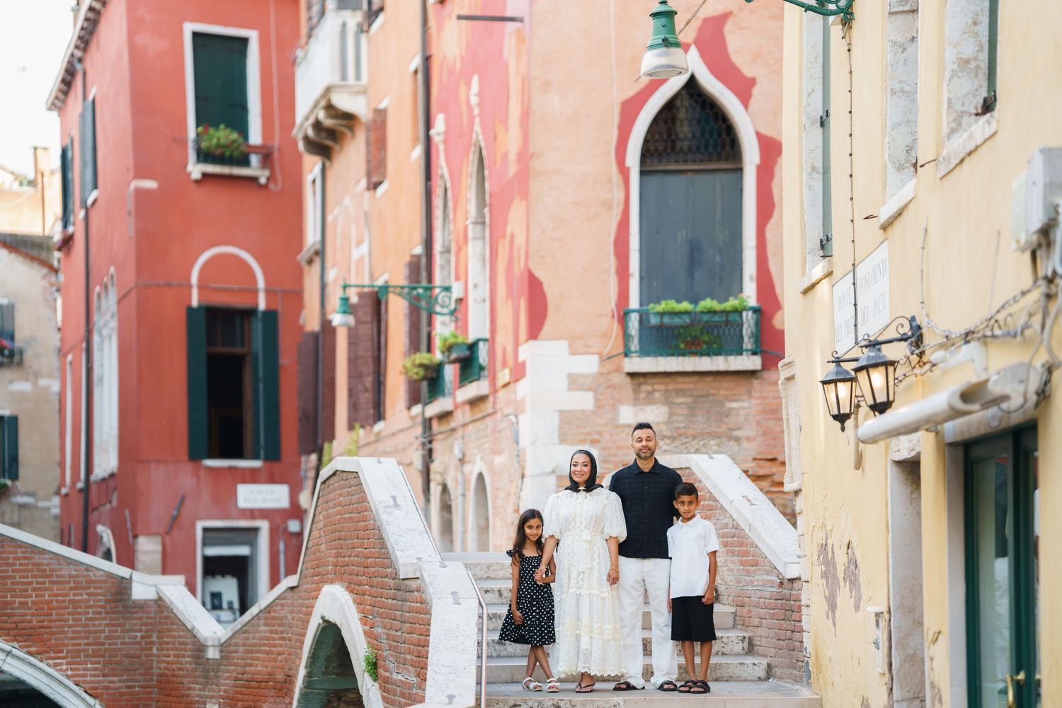 Family of four posing on a bridge in Venice, Italy, surrounded by colorful historic buildings.