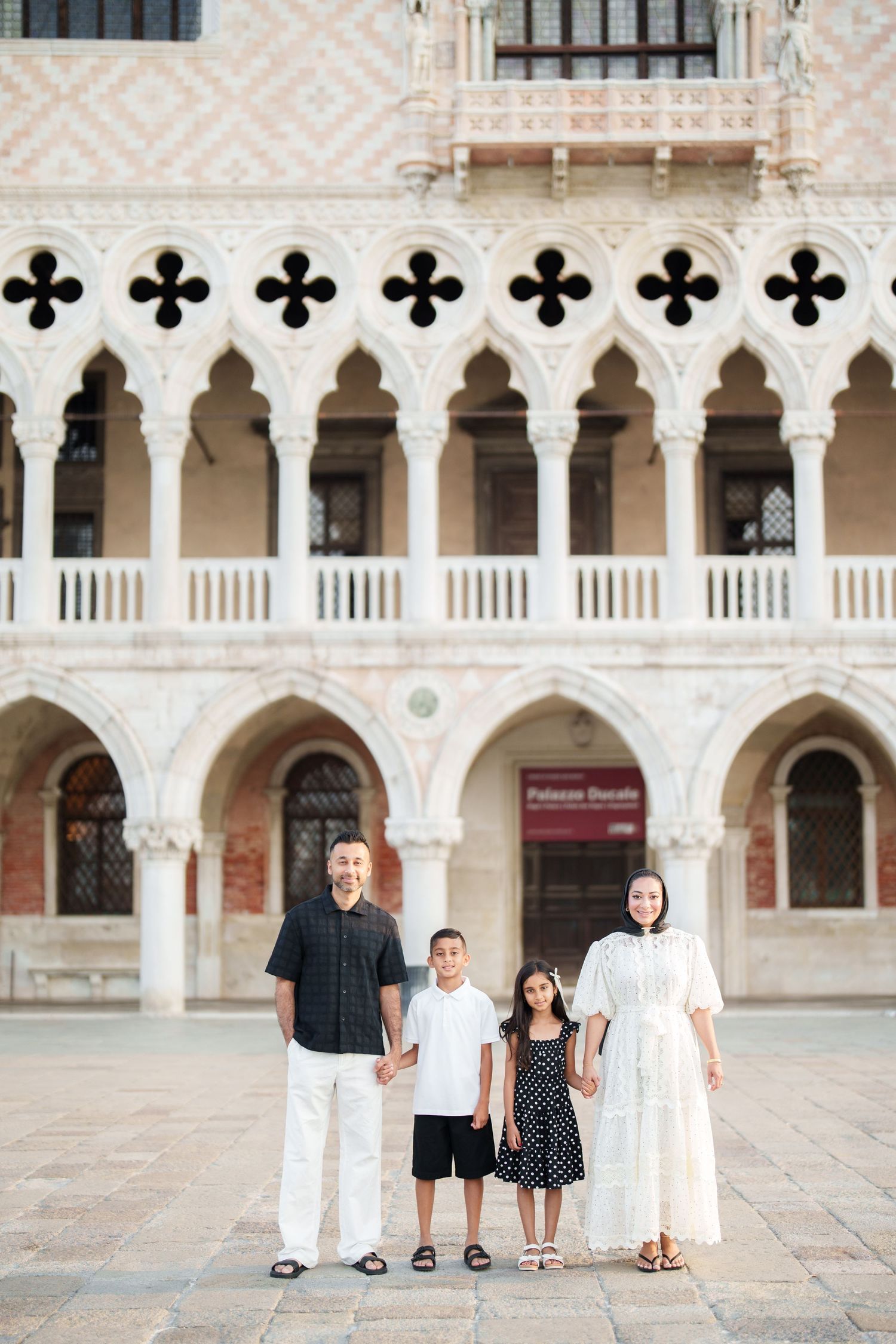 Family of four posing in front of the ornate Gothic architecture of Palazzo Ducale in Venice, Italy.