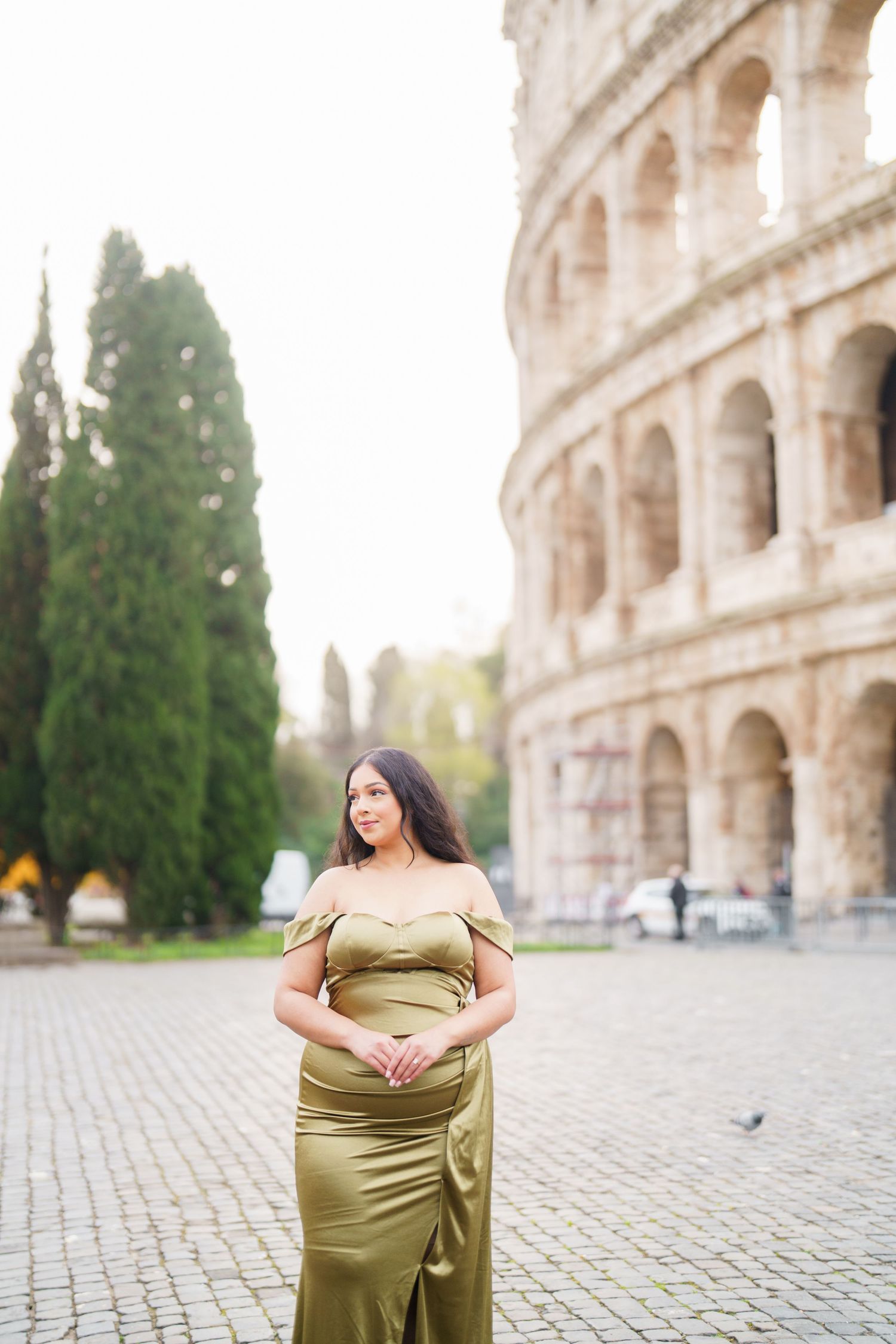 Pregnant woman in olive green gown posing in front of the Colosseum in Rome, Italy.