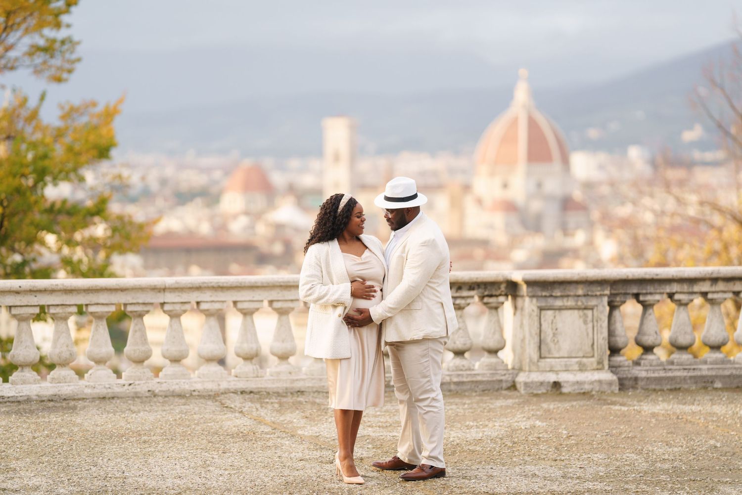 Elegant couple in white attire posing on a terrace with Florence skyline and Duomo cathedral backdrop.