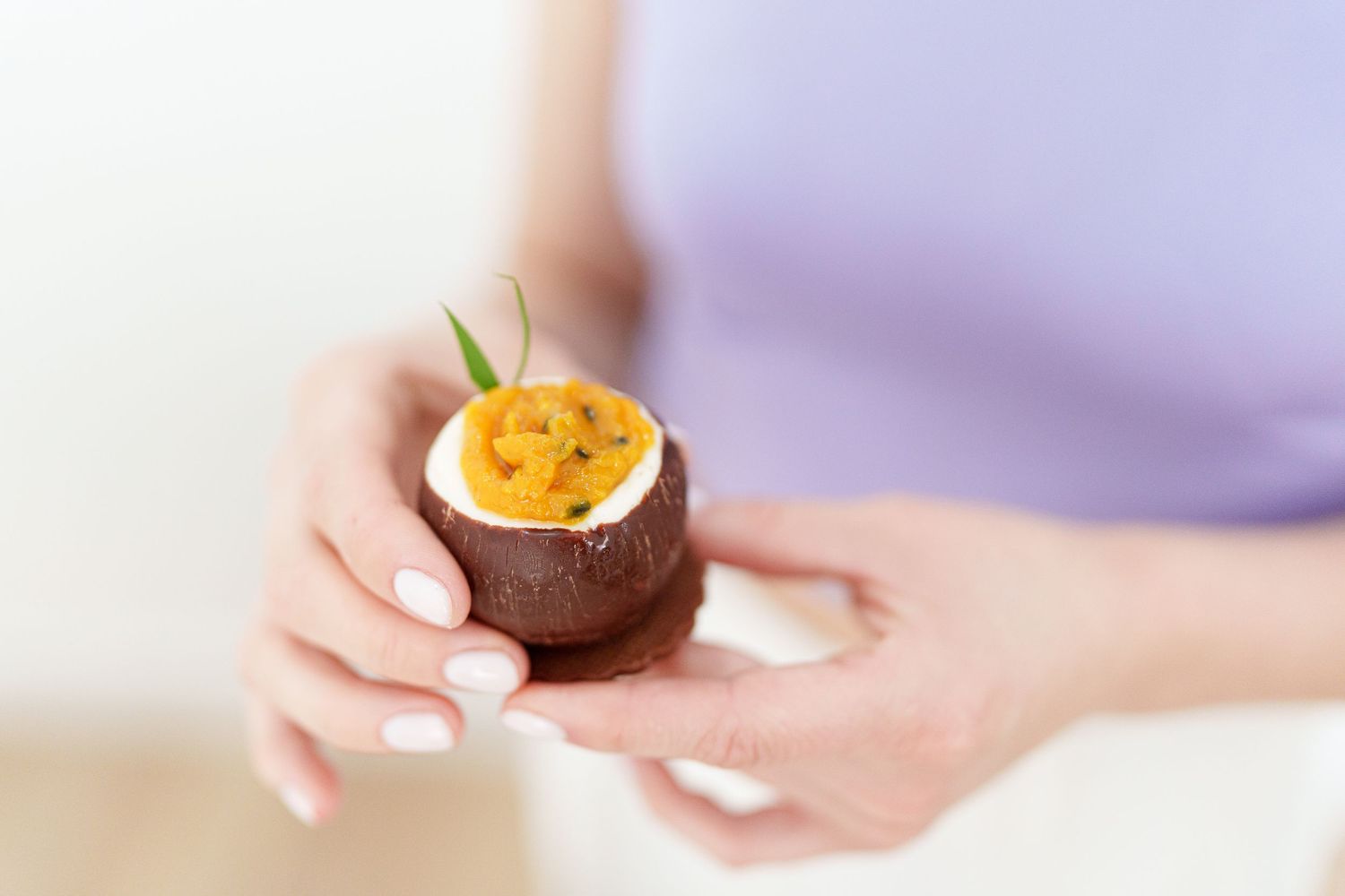 Woman holding a halved passion fruit chocolate dessert with green garnish on top.