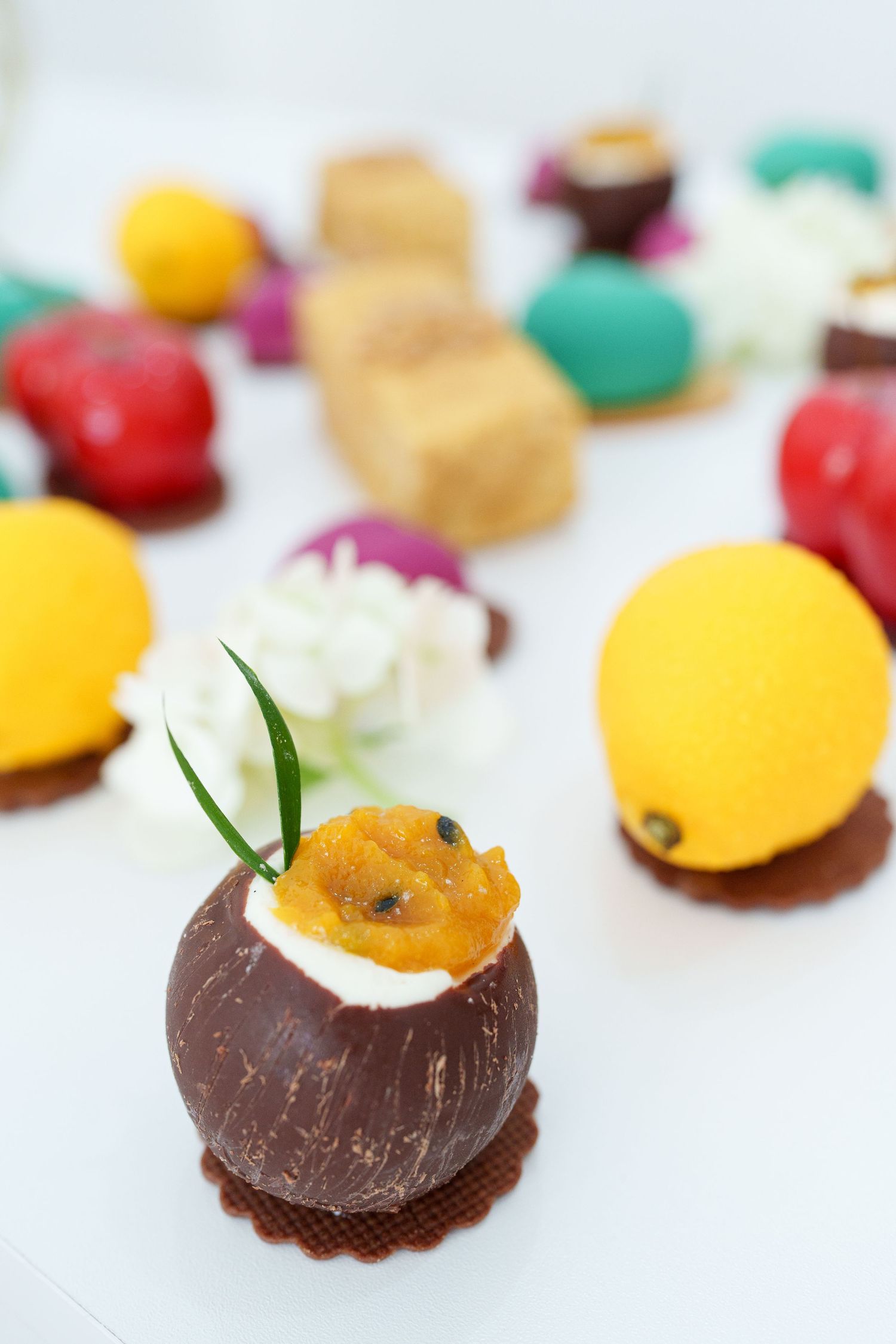 Assorted colorful chocolate truffles and candy-coated sweets displayed on a white surface, with a coconut shell dessert in the foreground.