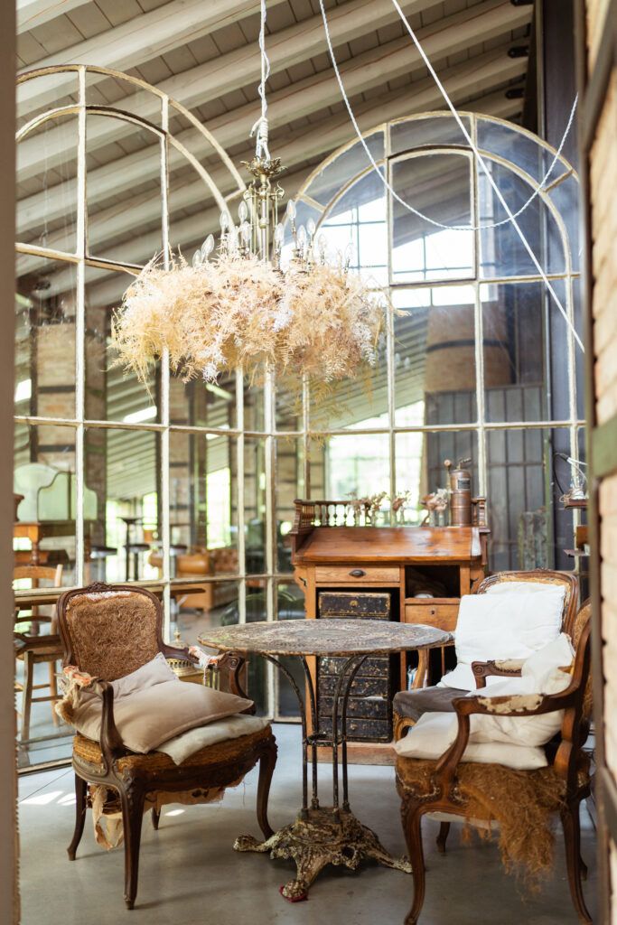 Elegant vintage seating area with ornate chairs and dried flower chandelier in sunlit conservatory.