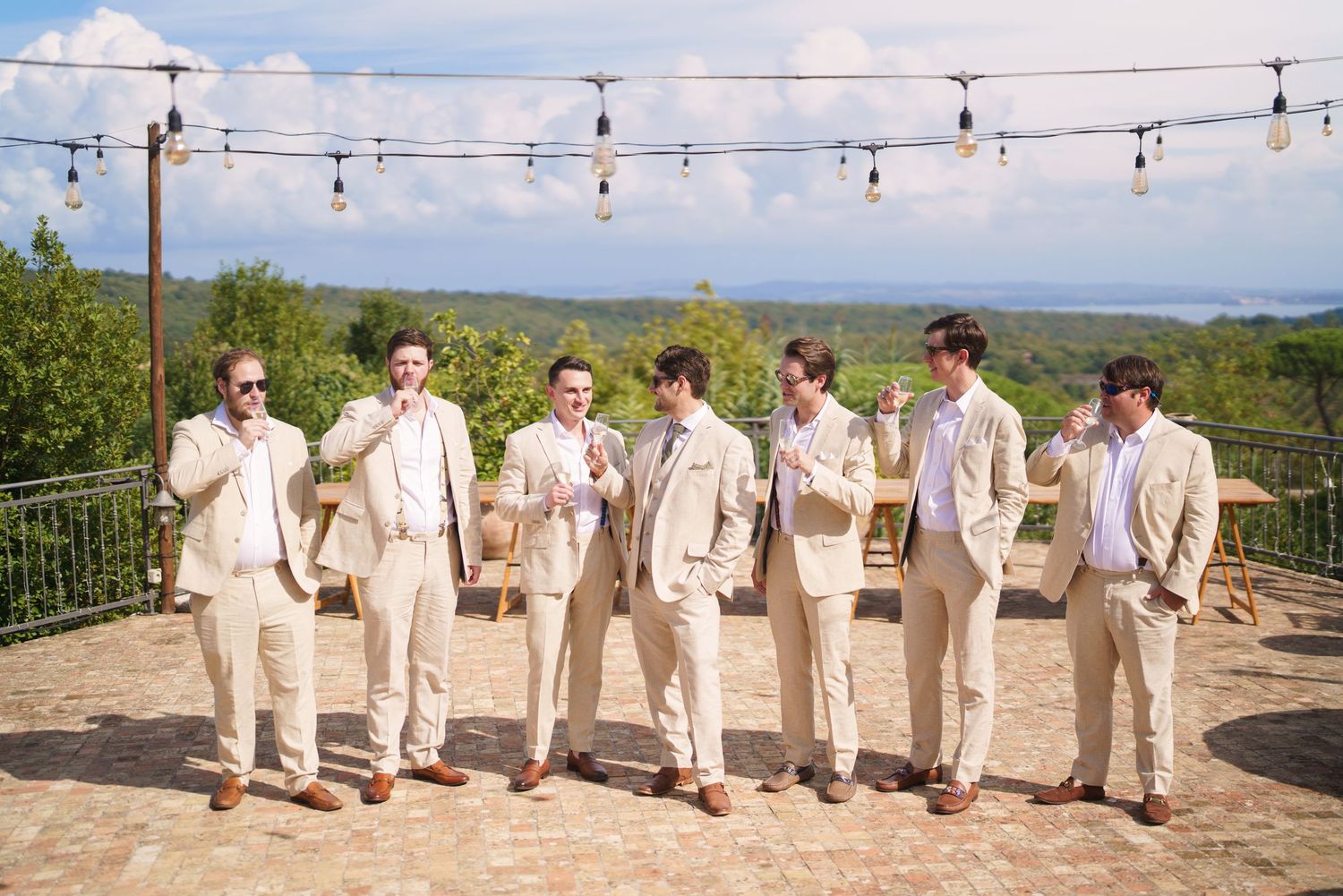 Wedding party in cream colored suits poses along an outdoor terrace with mountain views.