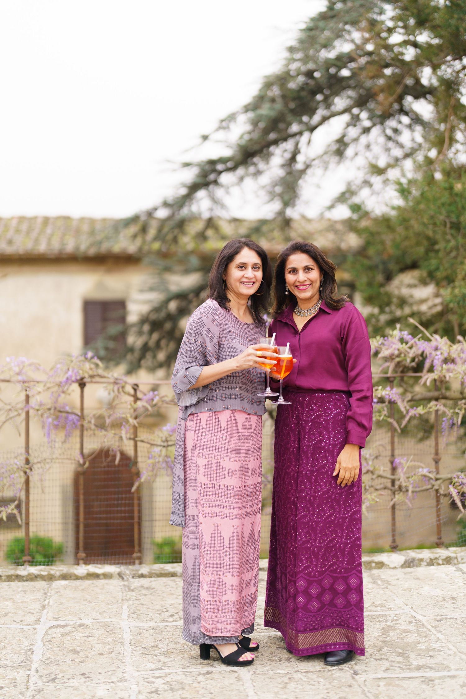 Two people in coordinating purple outfits stand together in a garden setting.