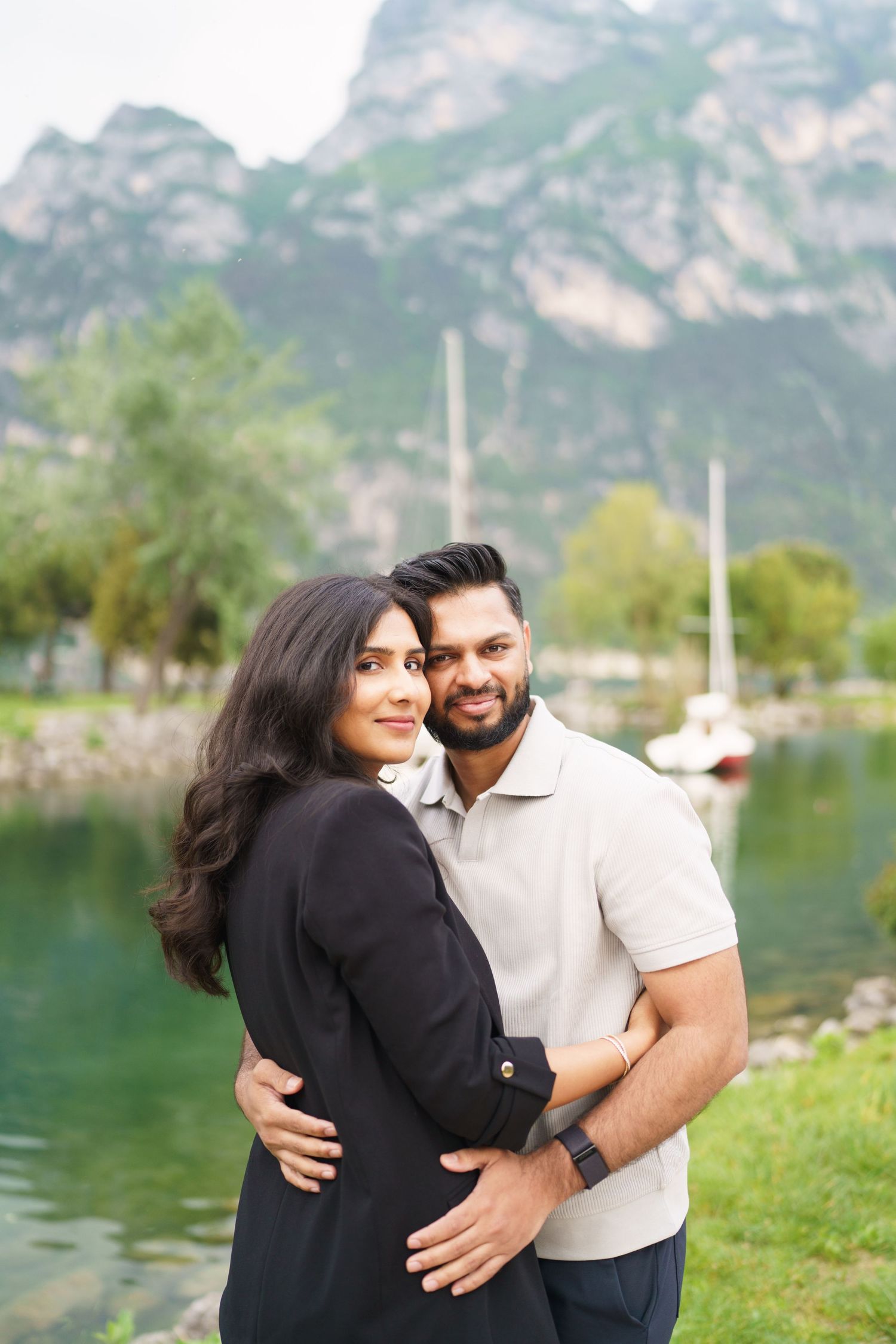A couple embraces lovingly by a scenic mountain lake with dramatic peaks in the background.