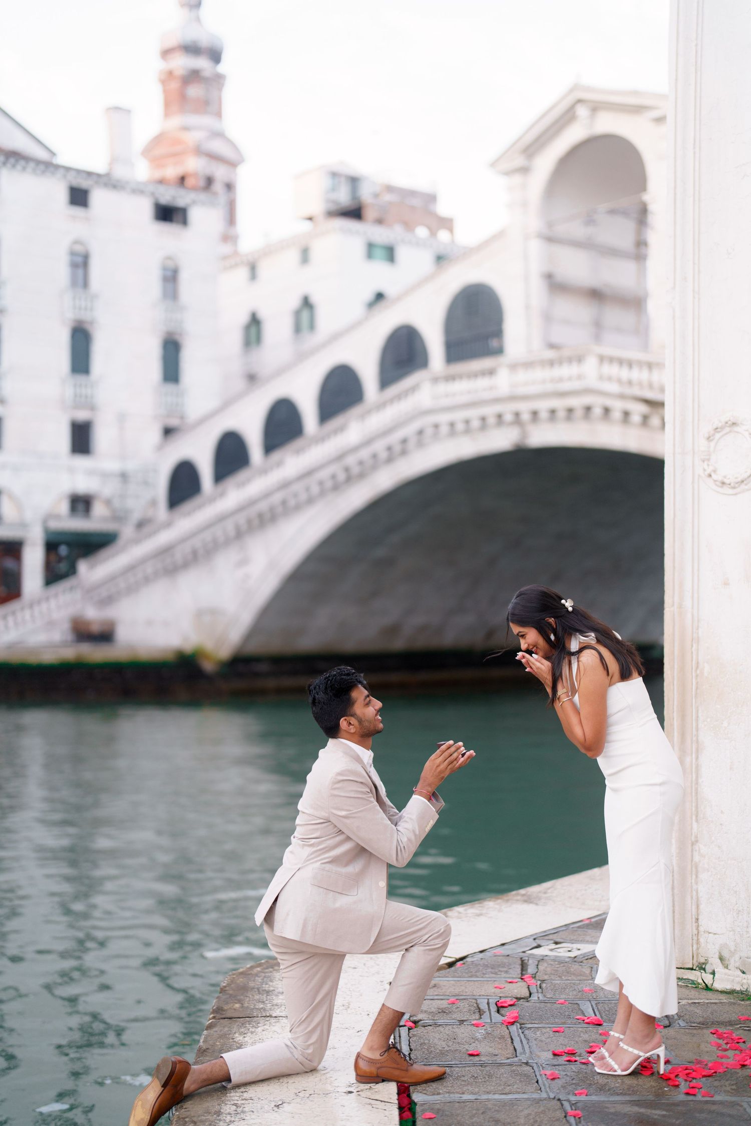 A romantic proposal moment unfolds along a Venetian canal with the iconic Rialto Bridge in the background.