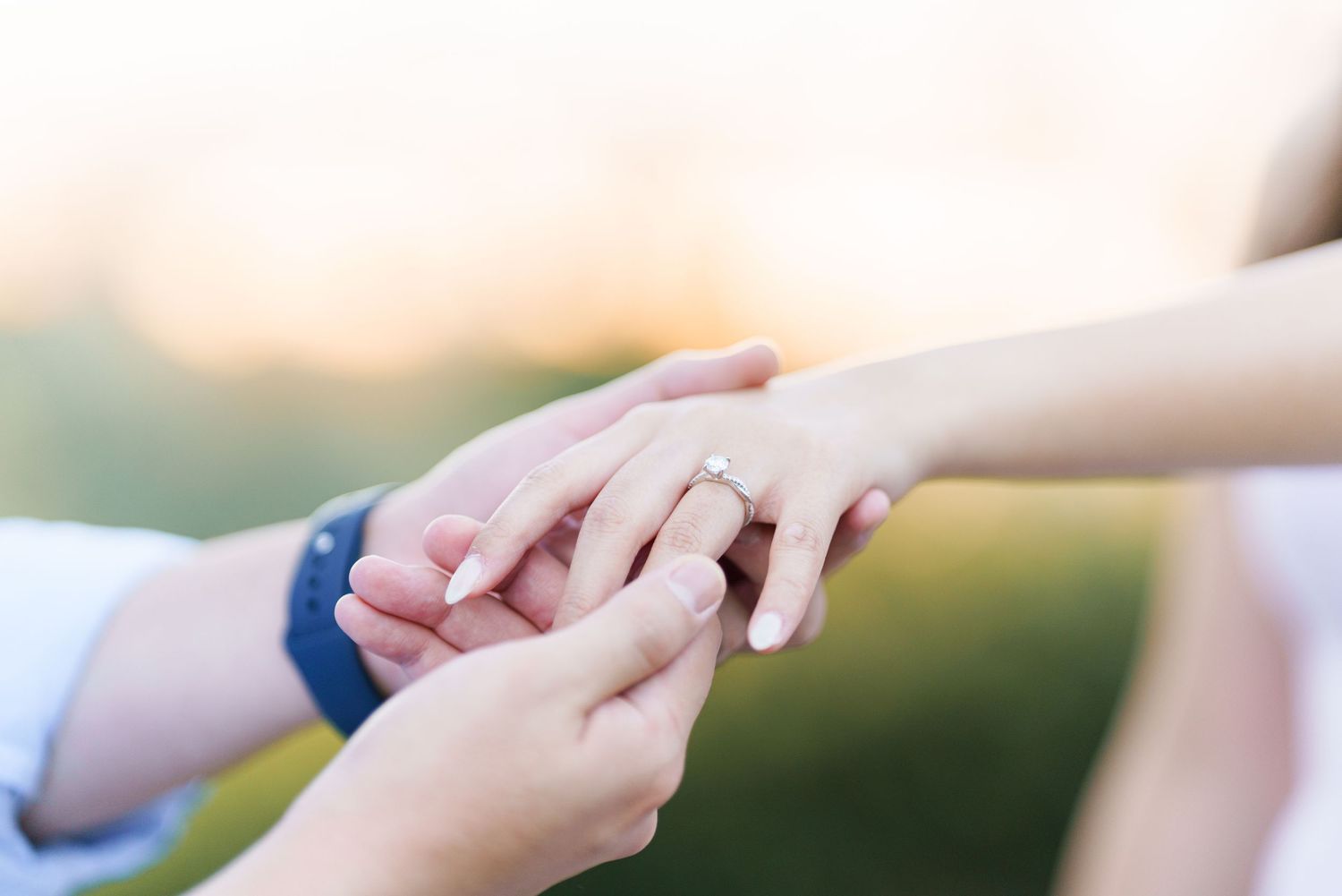 Two hands tenderly touch in a romantic moment against a soft blurred outdoor background.