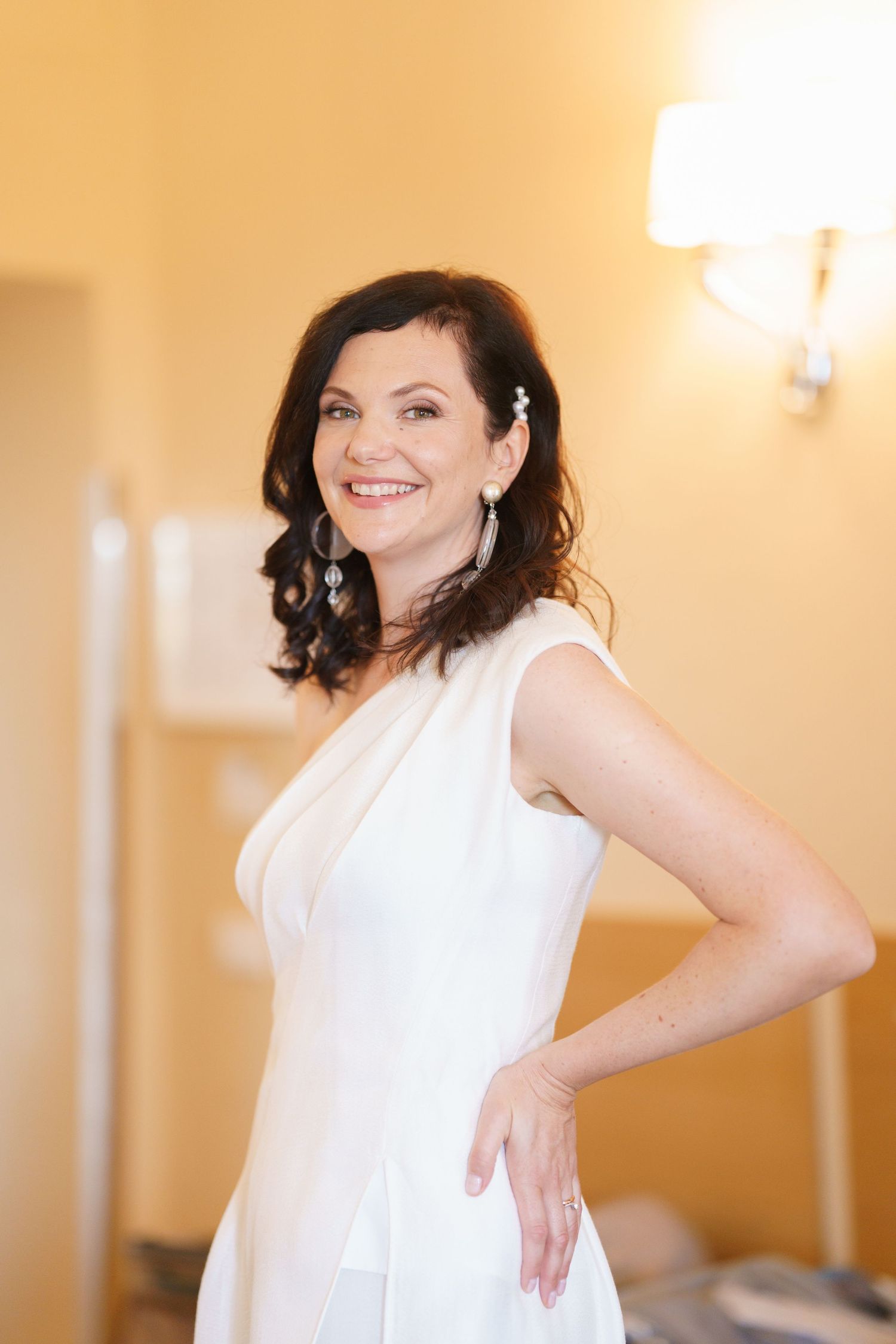 Woman in sleeveless white dress poses confidently in sequence against warm interior backdrop.