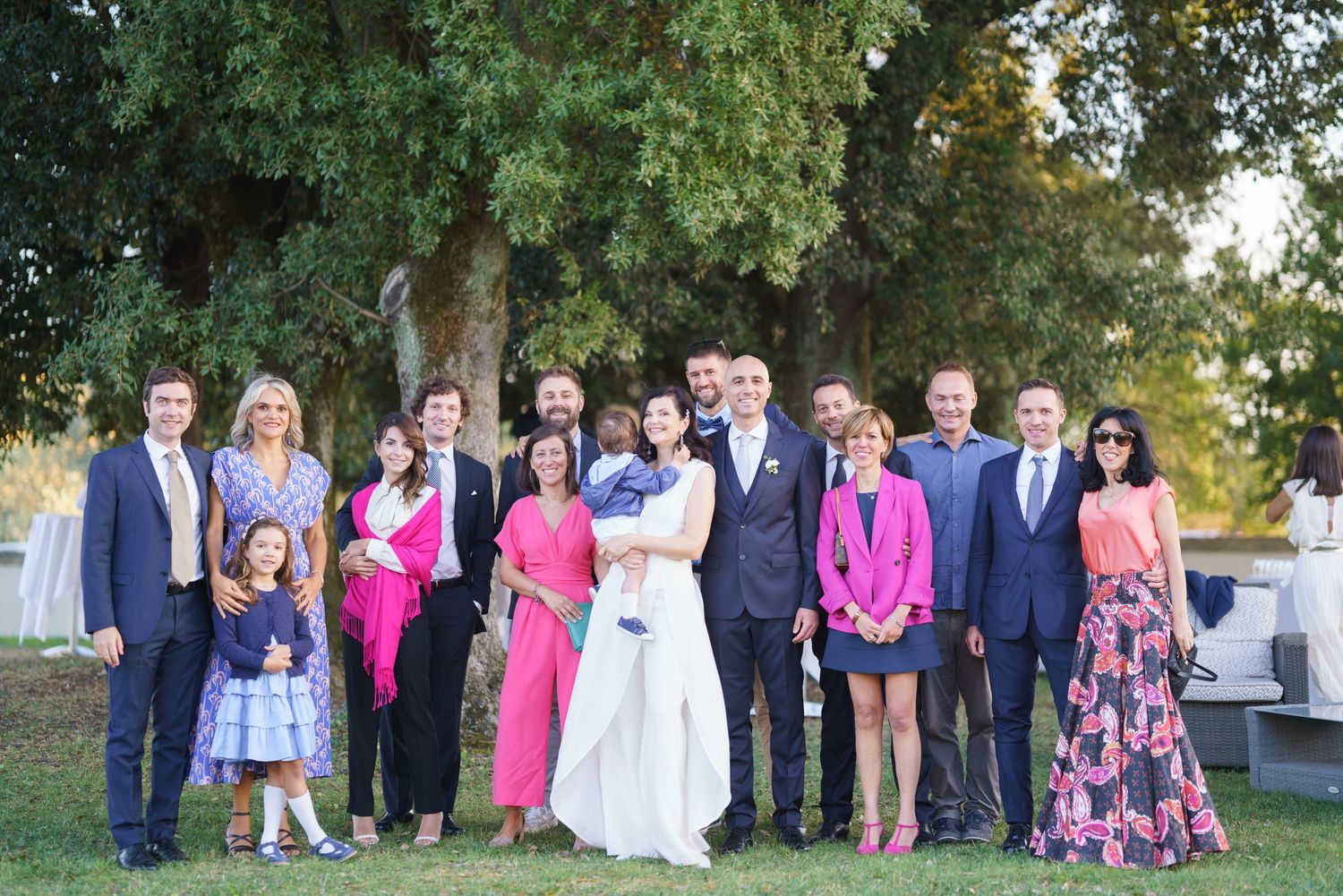 Formal group portrait of wedding party members in colorful attire standing outdoors.