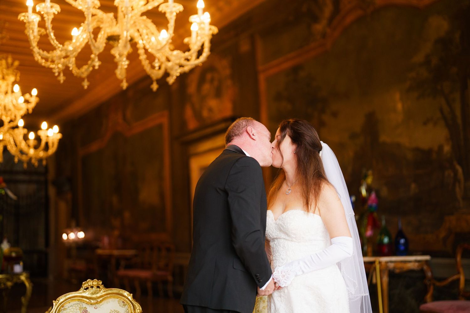 A couple shares their first dance as newlyweds under elegant crystal chandeliers in a dimly lit ballroom.