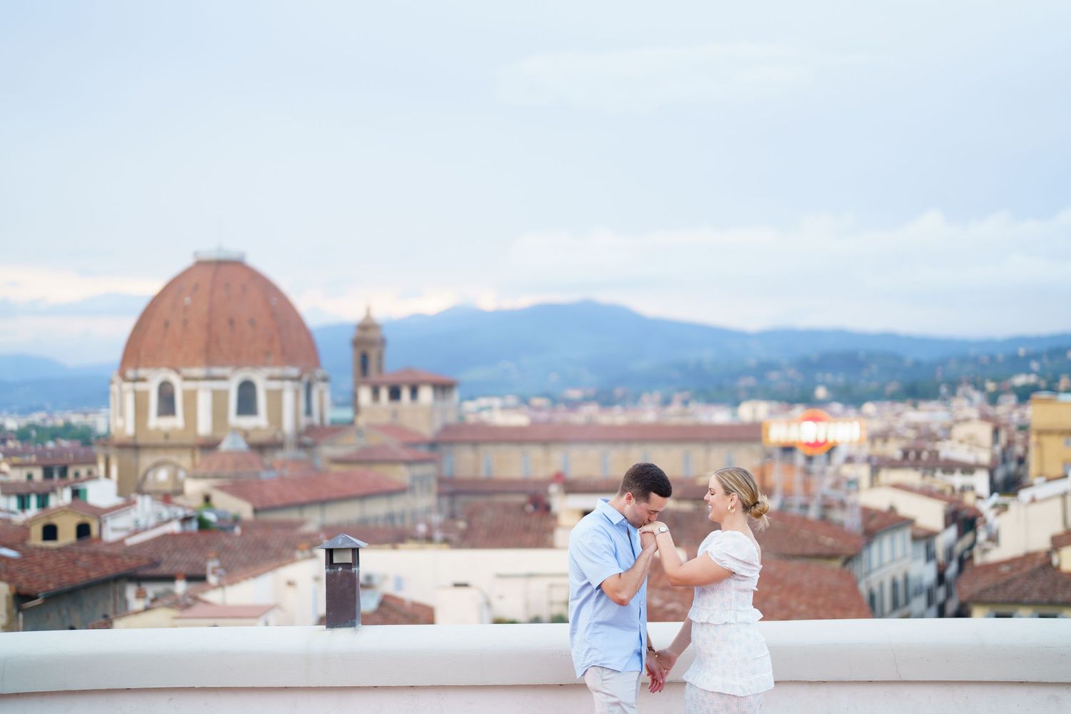 Panoramic view of Florence cityscape with historic domed buildings and mountains in the background under cloudy skies.