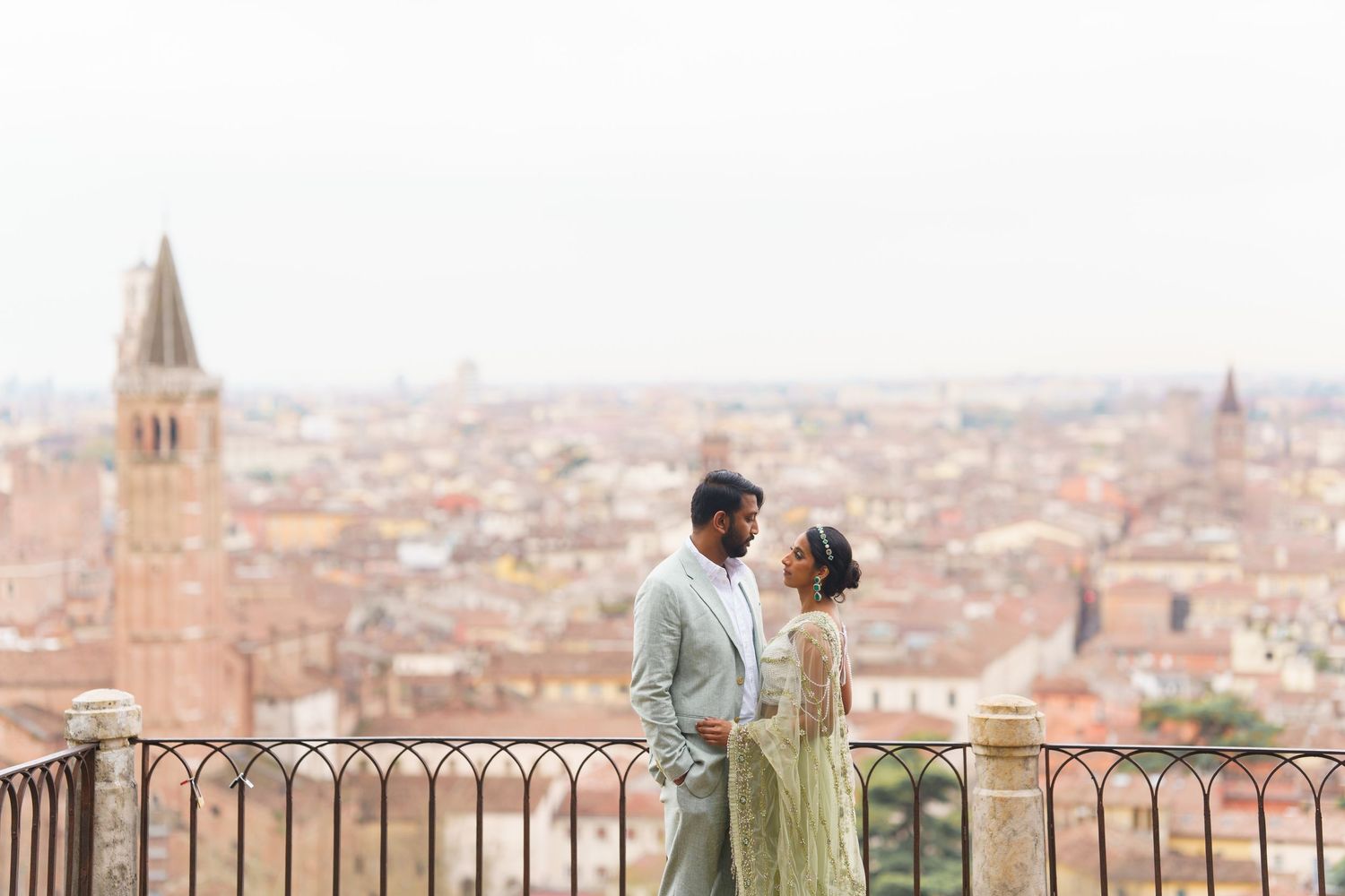 A couple shares a romantic moment overlooking the historic city skyline of Bologna, Italy from a scenic viewpoint.