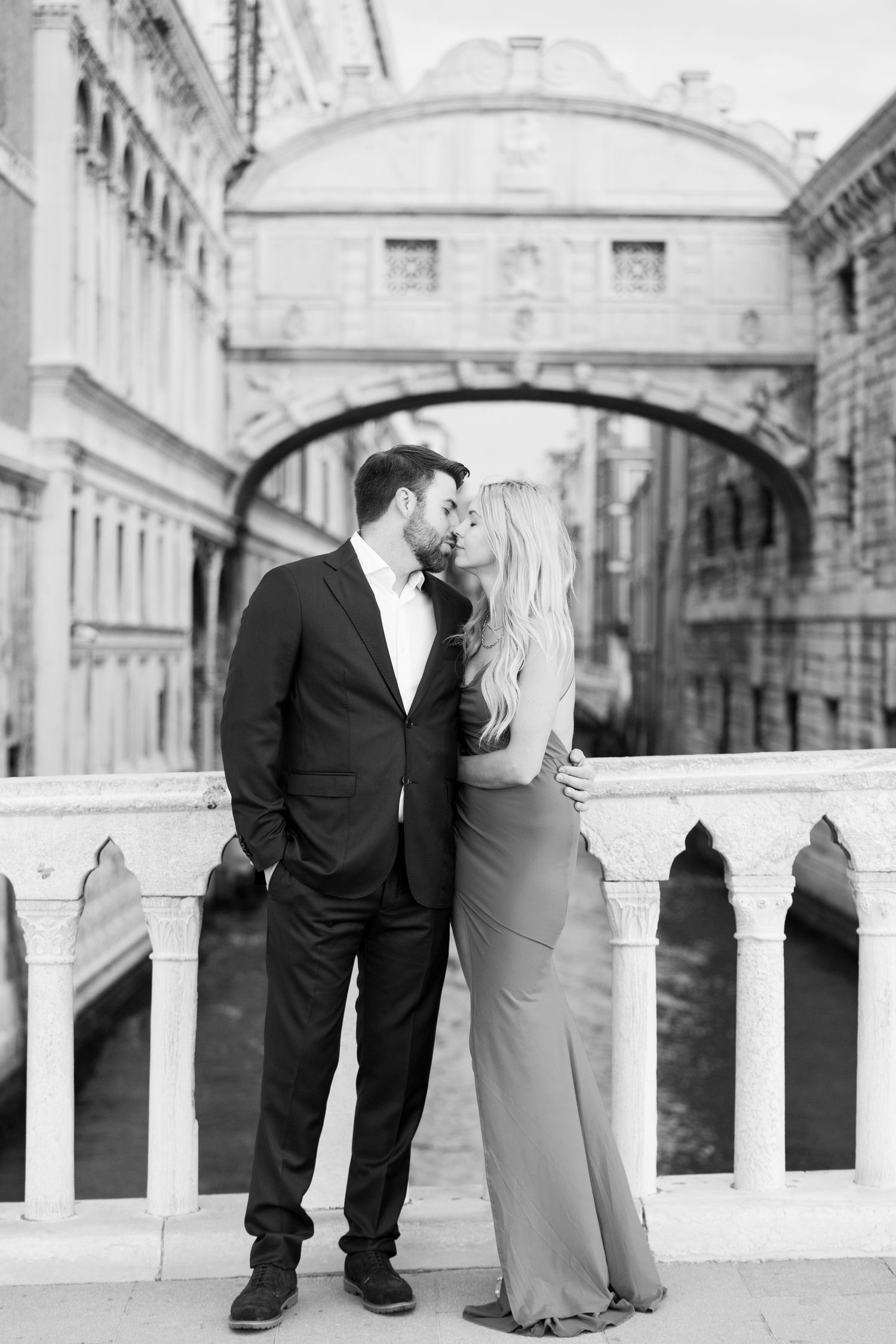 A romantic black and white photograph of a couple embracing at the Bridge of Sighs in Venice, Italy.