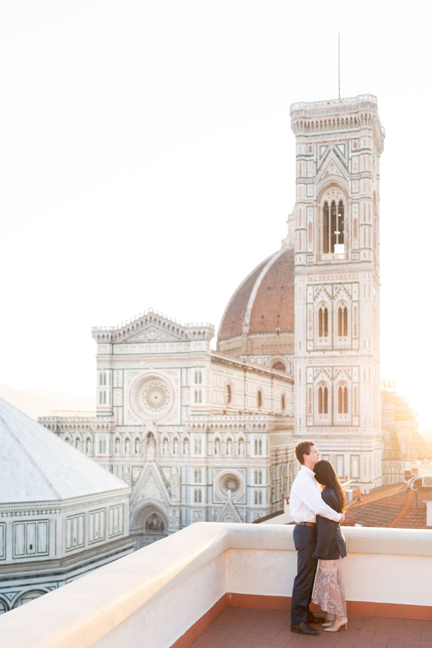 Couple embraces on rooftop terrace overlooking Florence Cathedral during golden sunset in Italy.