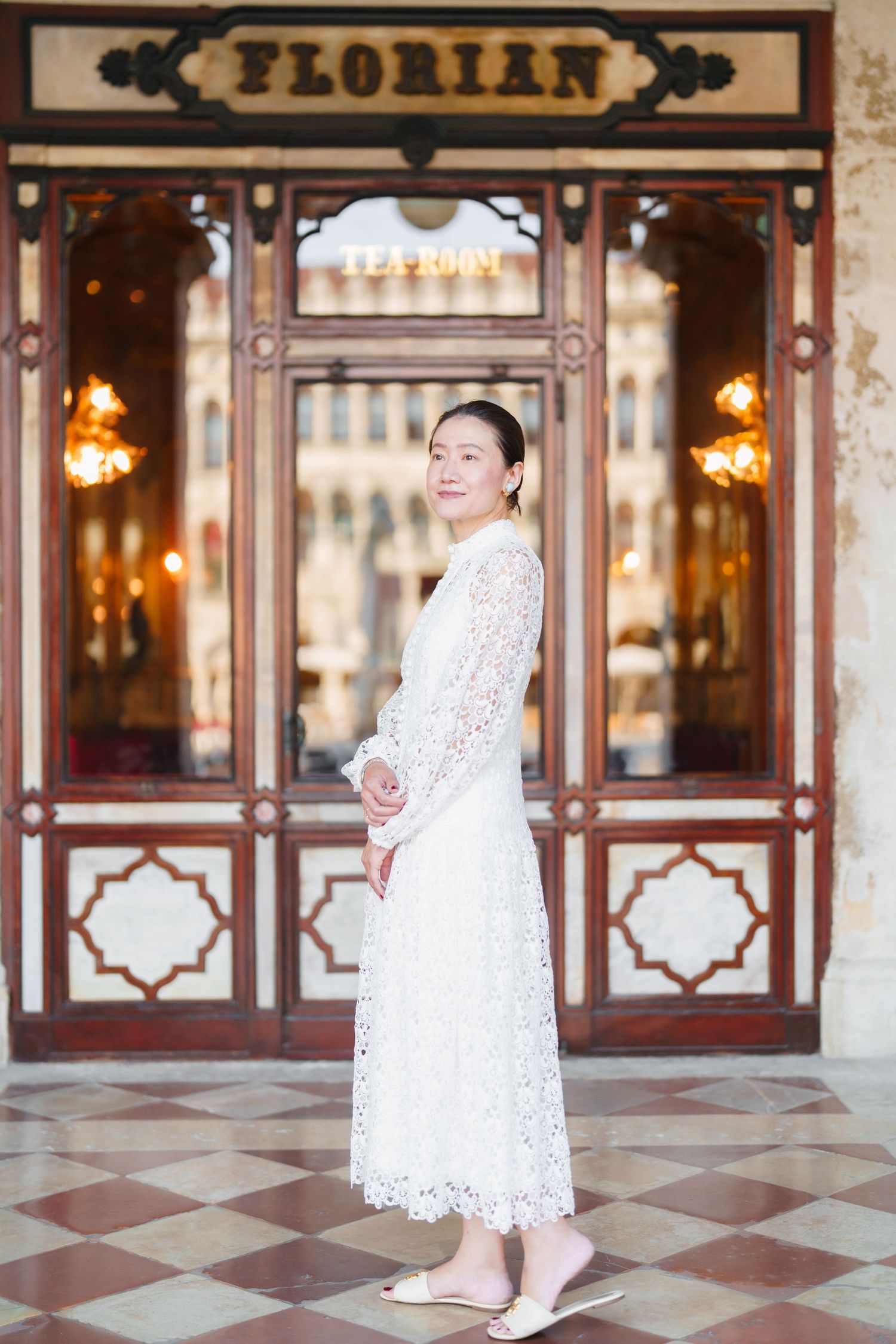 Woman in white lace dress posing outside Cafe Florian tearoom in Venice, Italy.