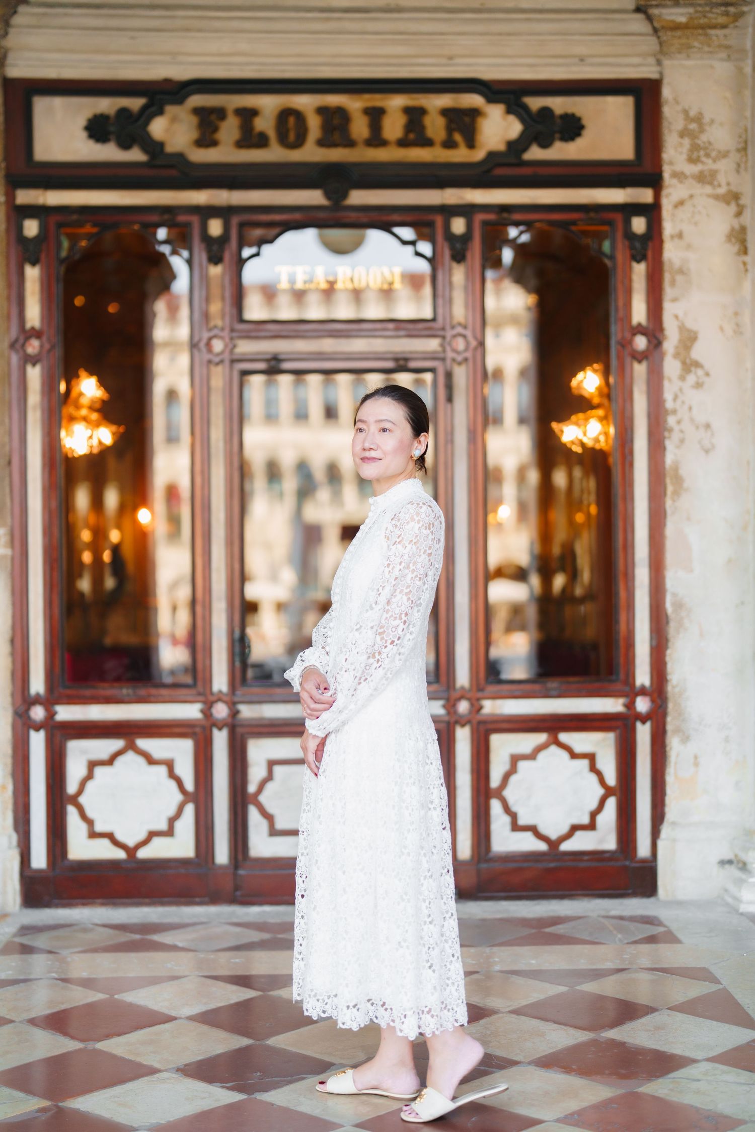 Woman in white lace dress posing outside Caffe Florian in Venice, Italy.