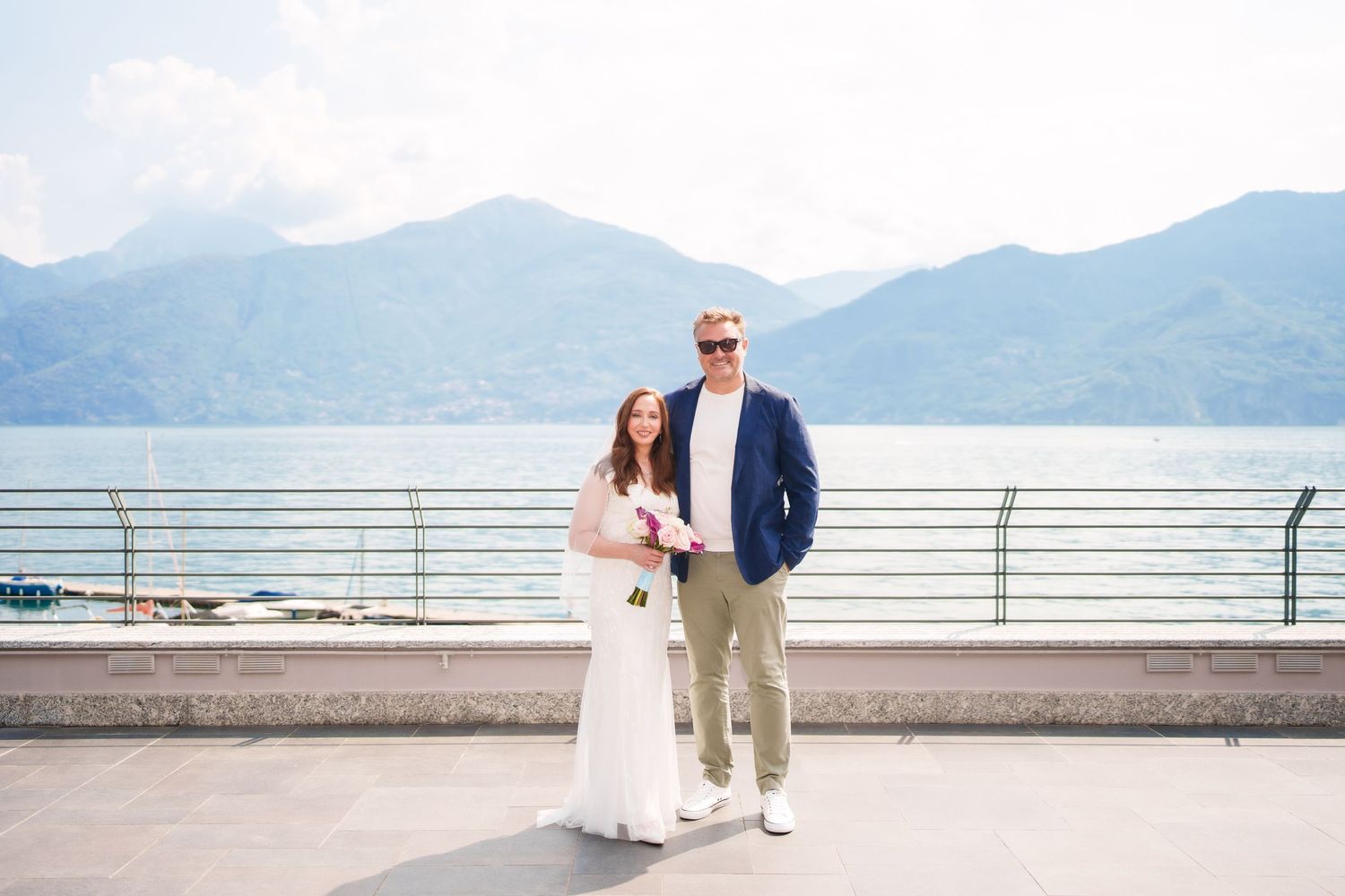 Bride and groom posing on a lakeside terrace with mountain views at Lake Como, Italy wedding.