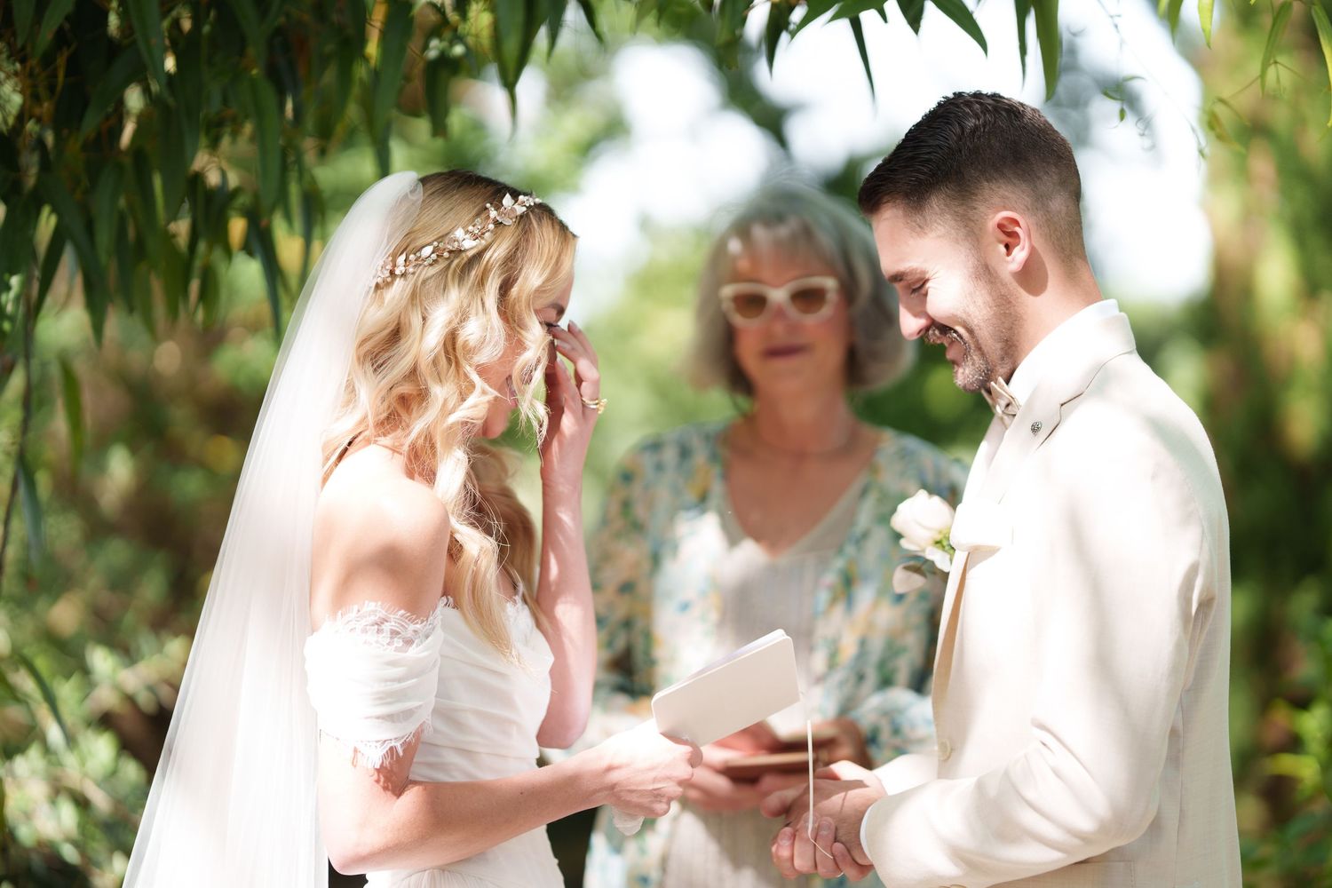 Emotional outdoor wedding ceremony with bride and groom exchanging vows while officiant stands behind them.