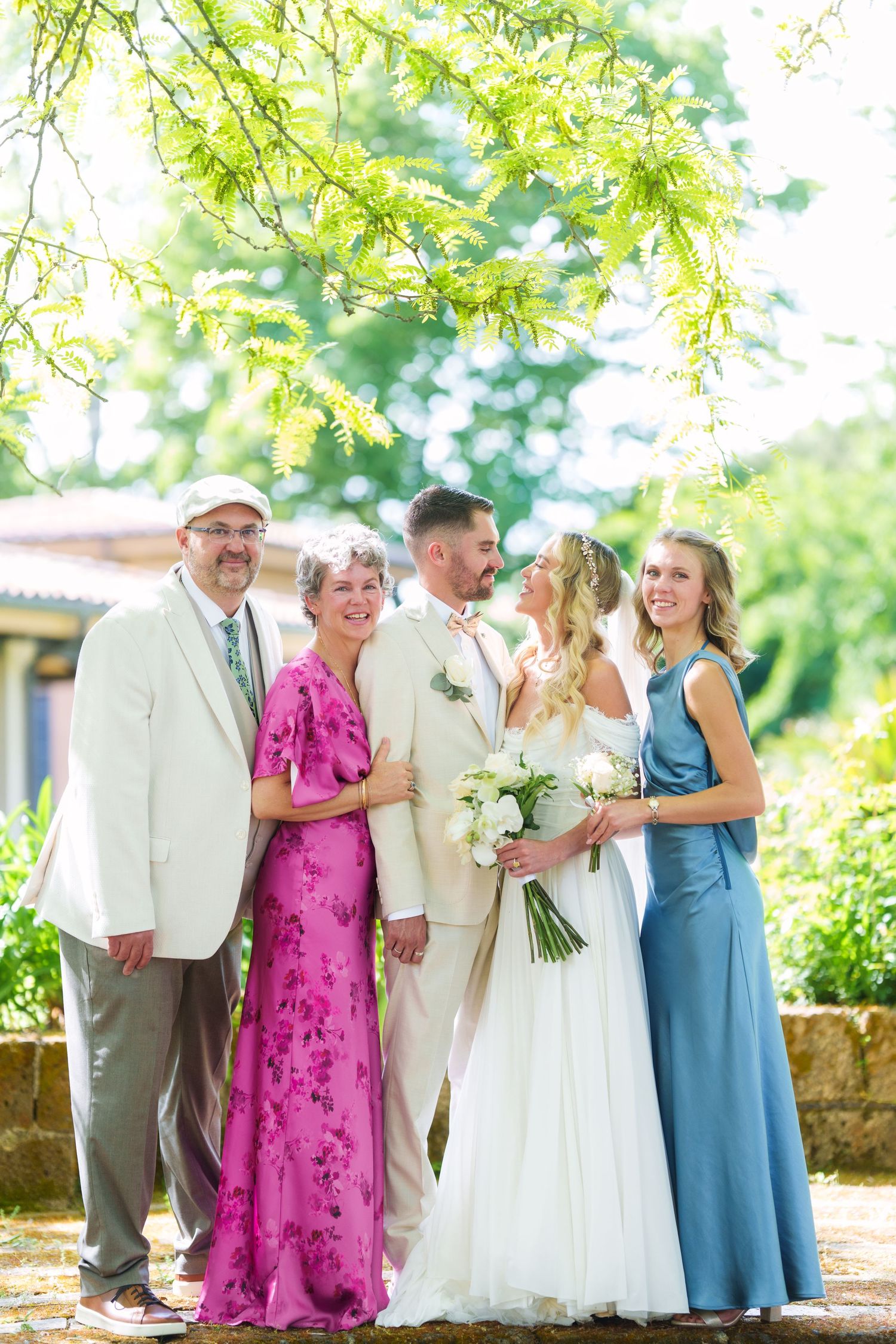 Wedding party poses outdoors under green trees, bride in white Italian lake wedding photographer