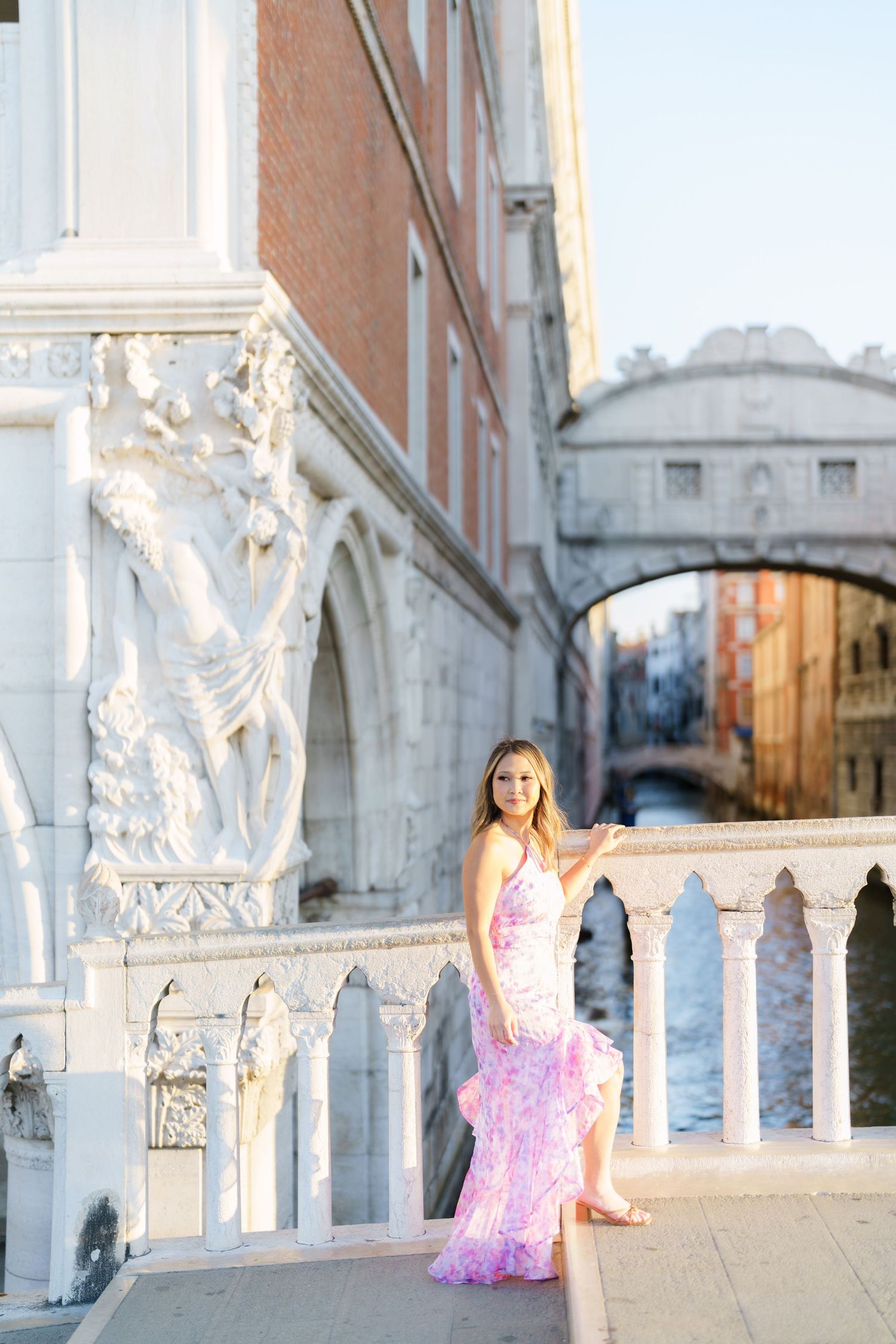 Young woman in pink ruffle gown posing near Bridge of Sighs in Venice, Italy at golden hour.