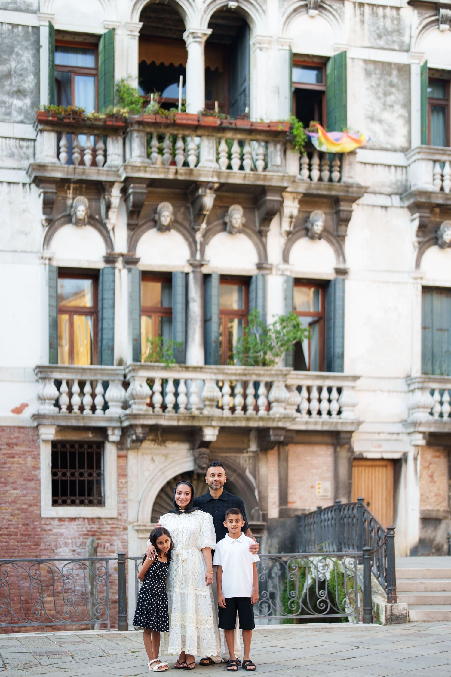 Family of four posing in front of ornate Venetian building with balcony and arched windows in Venice, Italy.