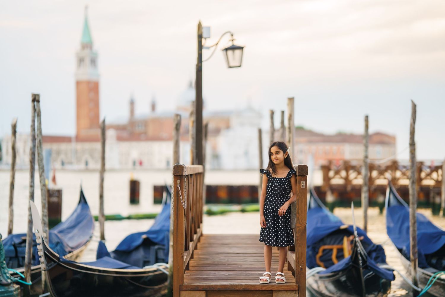 Young woman in polka dot dress standing on Venice gondola dock with San Giorgio Maggiore church in background.