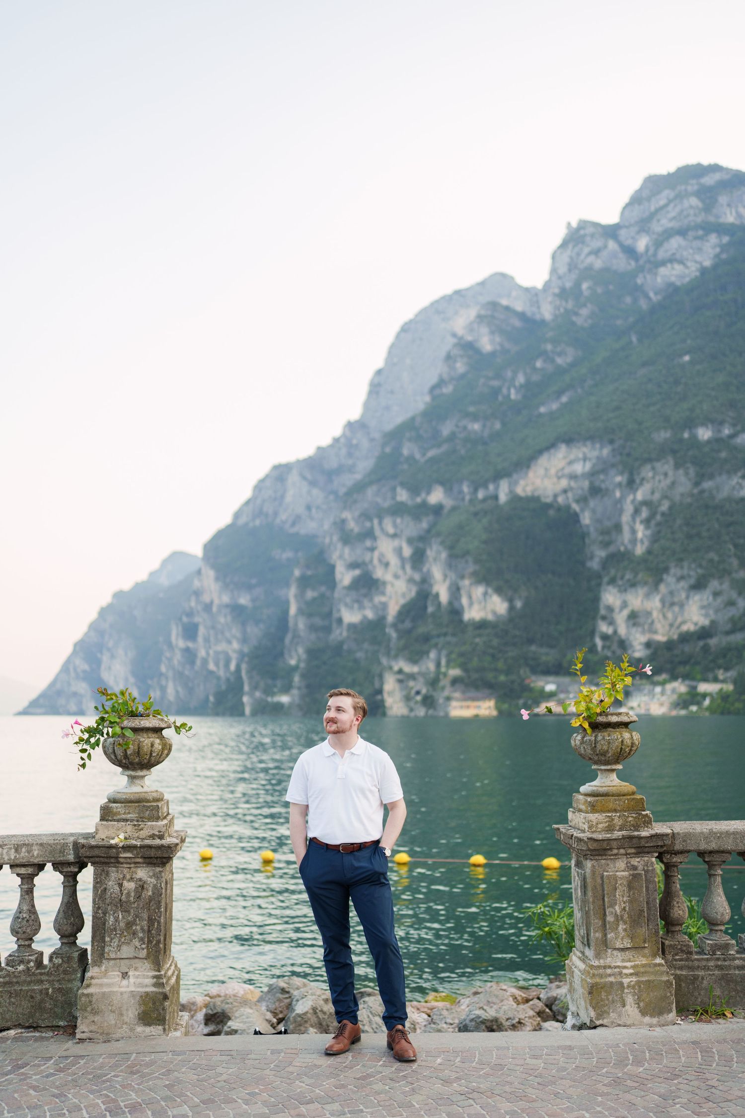 Man in smart casual attire gazing at stunning Lake Garda scenery from ornate stone terrace balcony.
